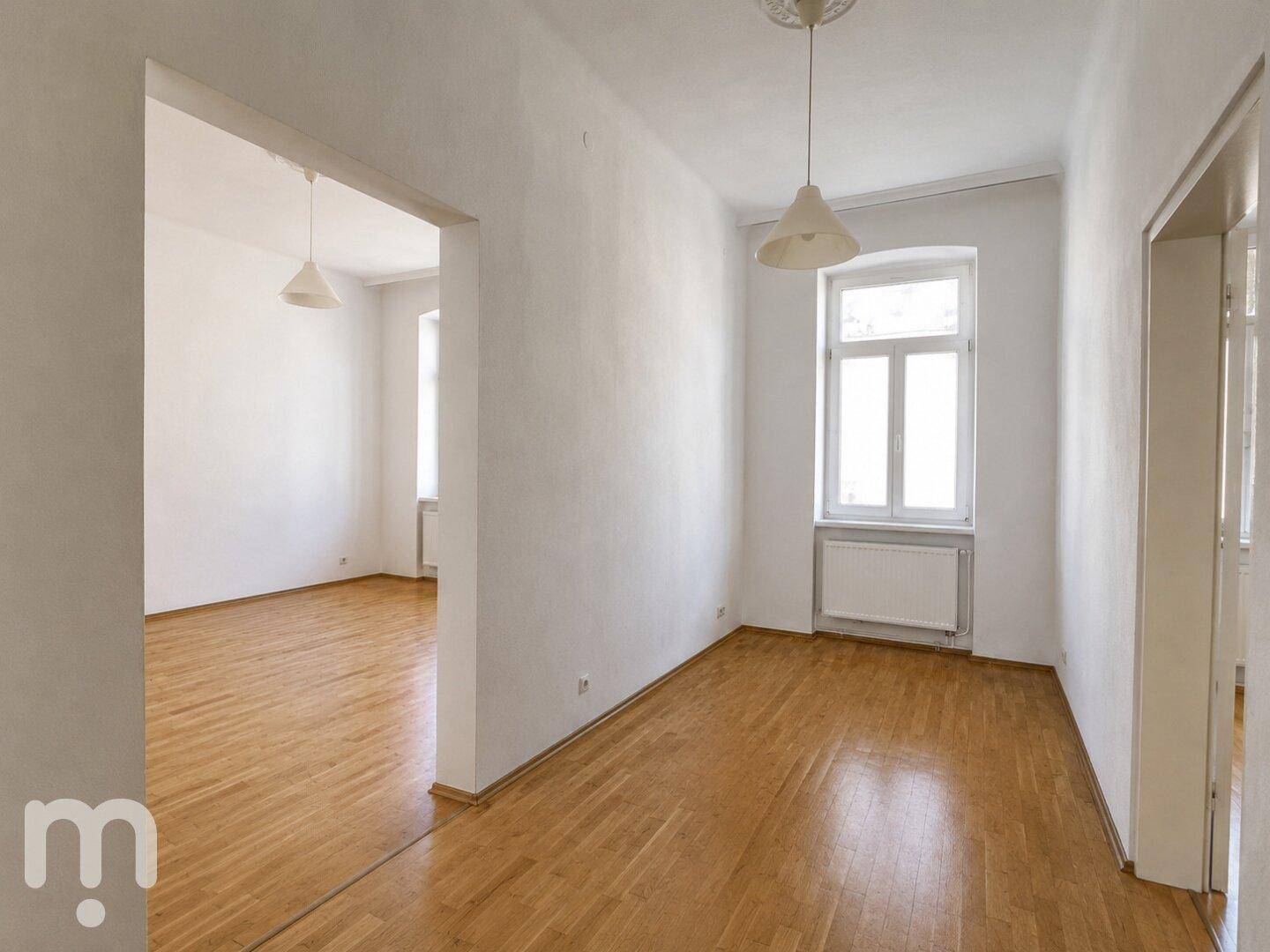 Großes, helles Zimmer mit Parkettboden und offenem Übergang zu einem weiteren Raum.