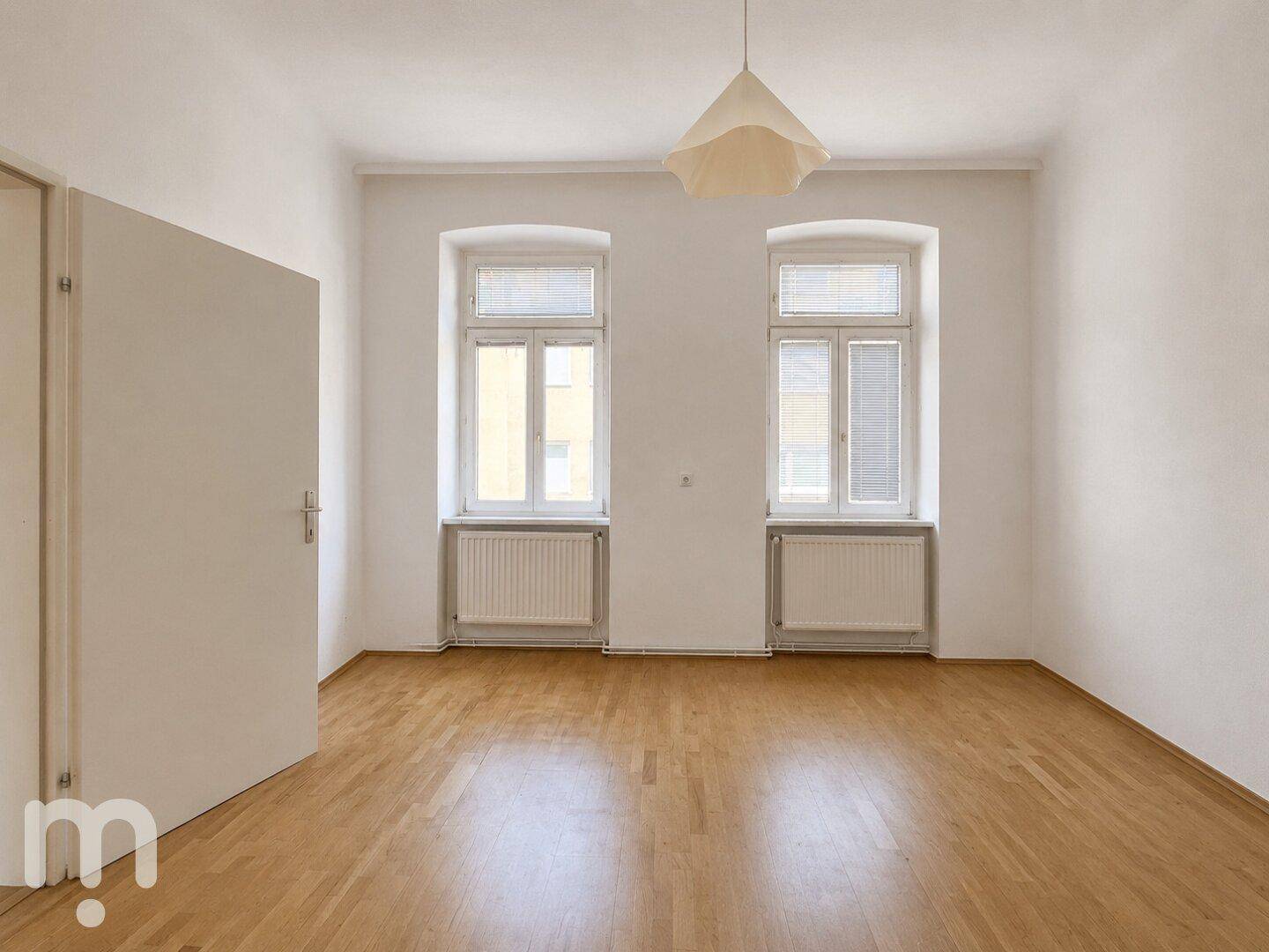 Leeres Schlafzimmer mit Parkettboden und zwei Fenstern, bereit für eine persönliche Einrichtung.