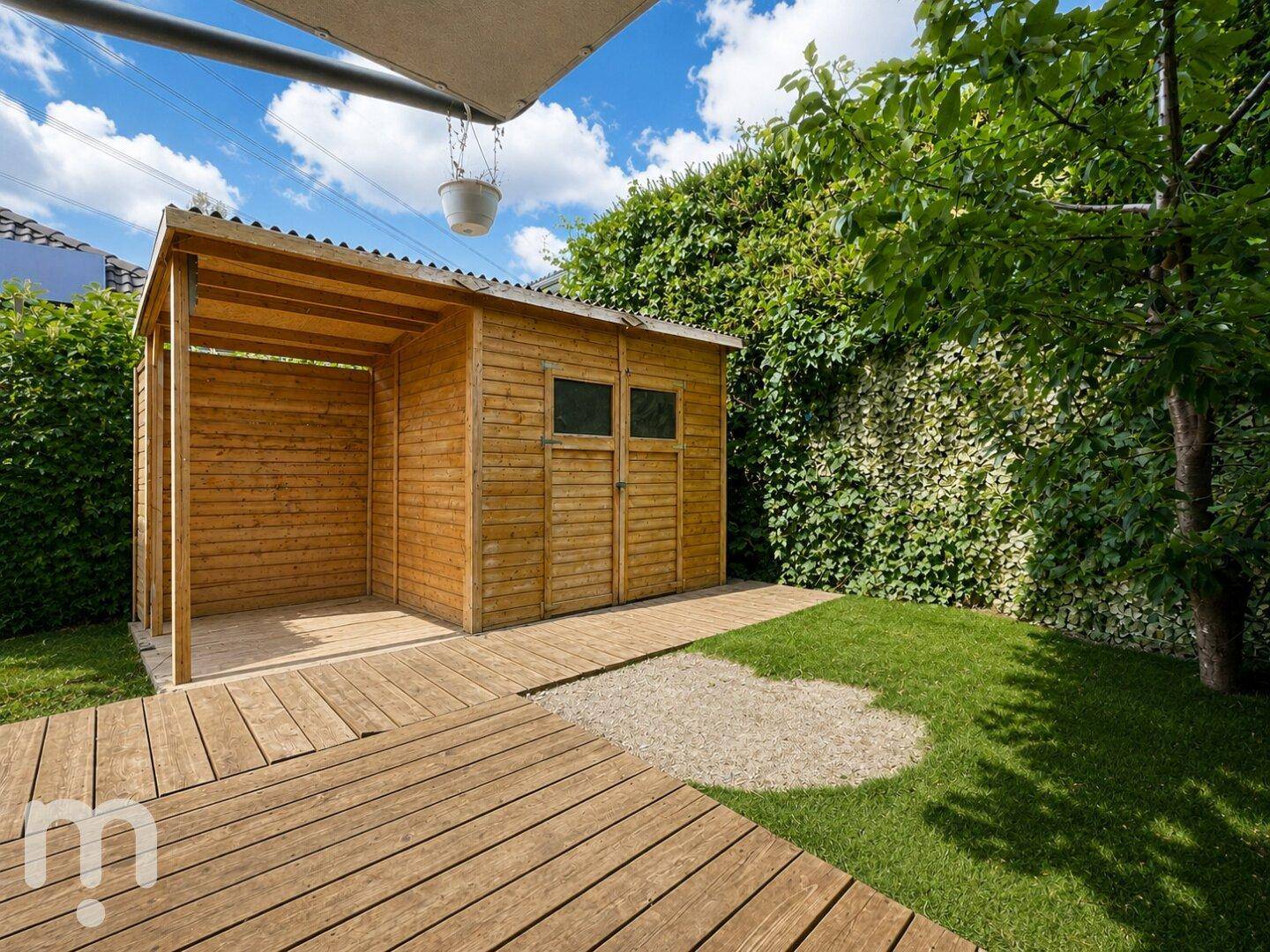 Gartenhaus aus Holz mit überdachtem Bereich und Holzweg, umgeben von viel Grün.