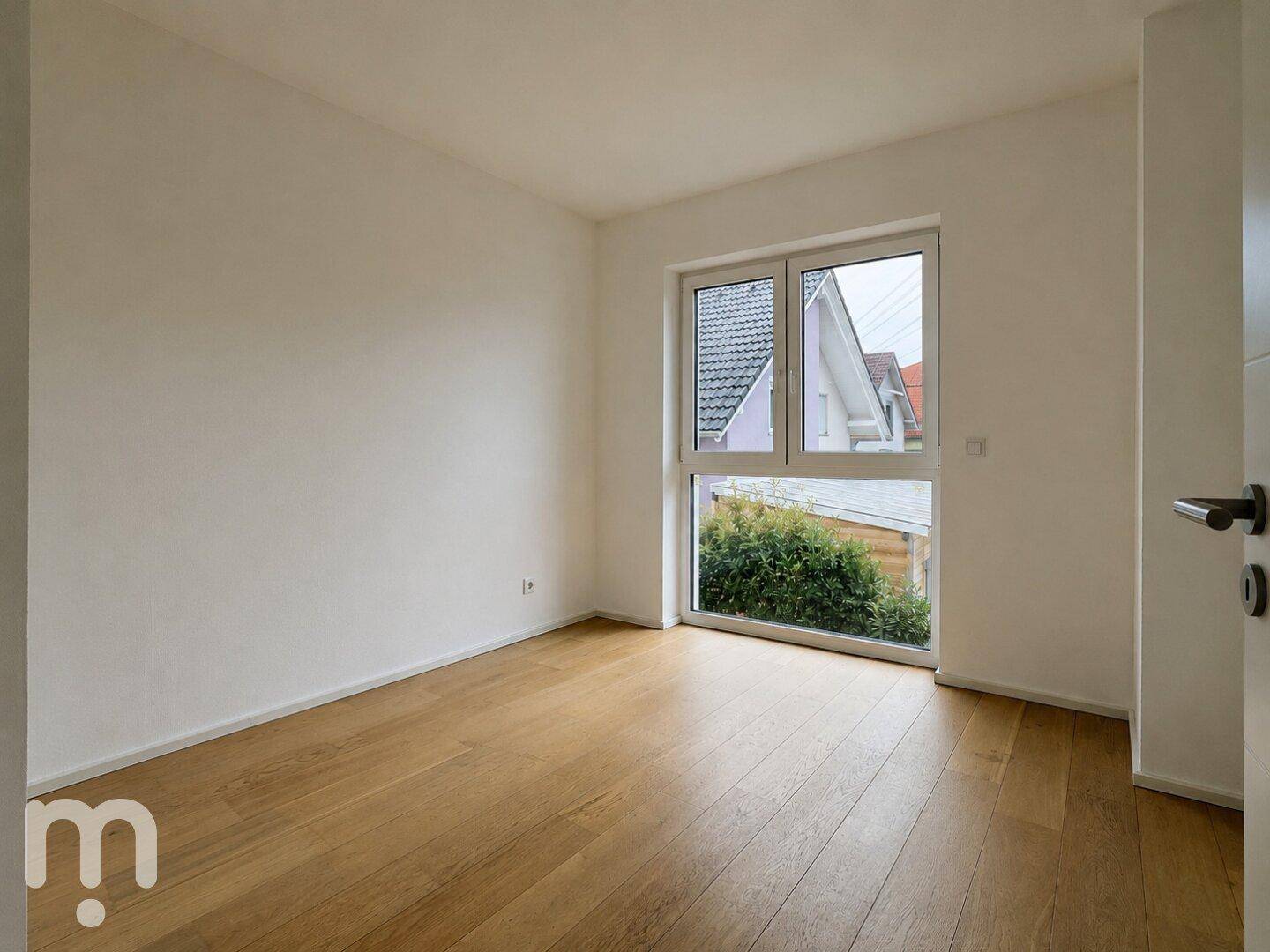 Ruhiges Zimmer mit Holzboden und Fenster, das einen Blick ins Grüne bietet.