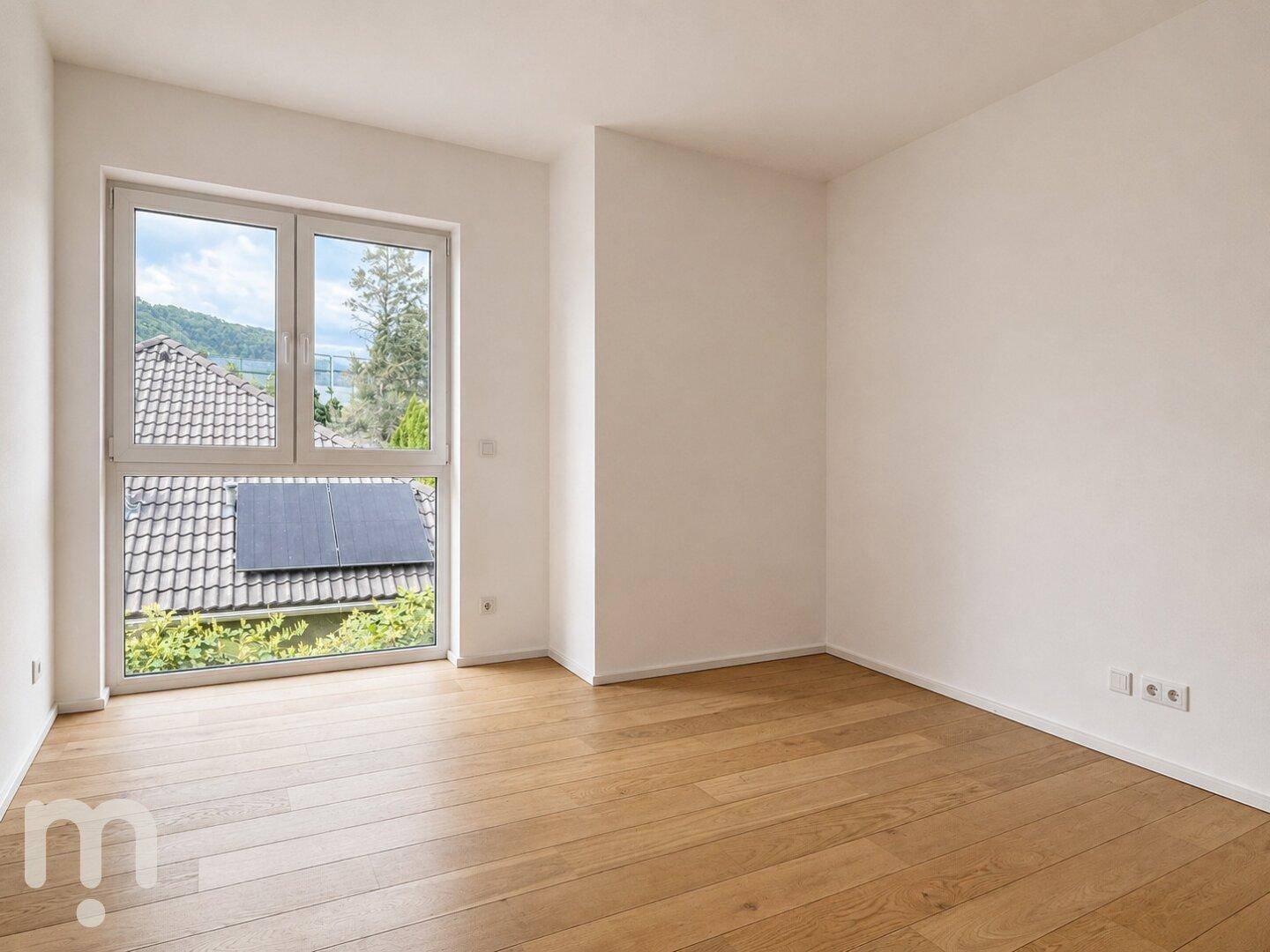Helles Zimmer mit Holzboden und Fenster mit Blick auf die umliegende Landschaft.