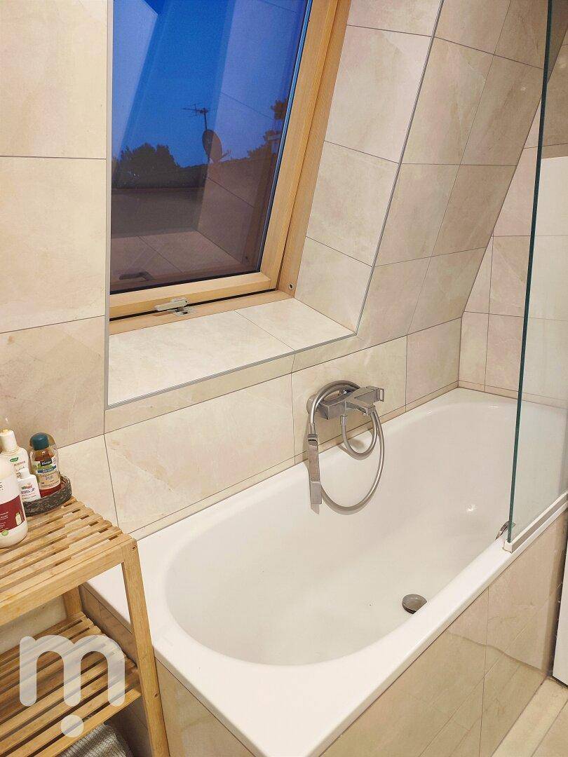 Badezimmer im Dachgeschoss mit Badewanne und Dachfenster, hell gefliest.