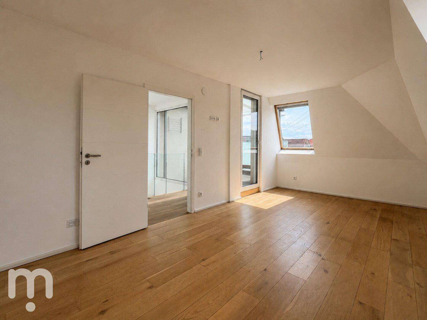 Helles Dachgeschosszimmer mit Holzboden, Dachfenster und Zugang zu einem Balkon.