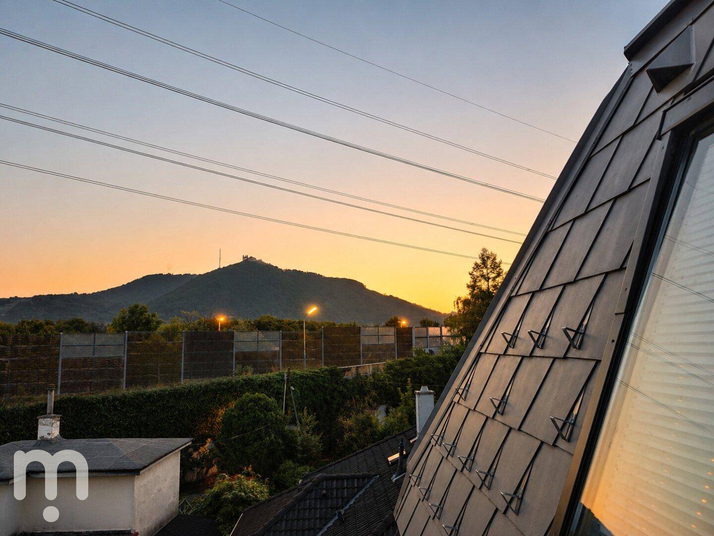 Abendlicher Blick auf die umliegende Berglandschaft mit Sonnenuntergang und Dachfenster.