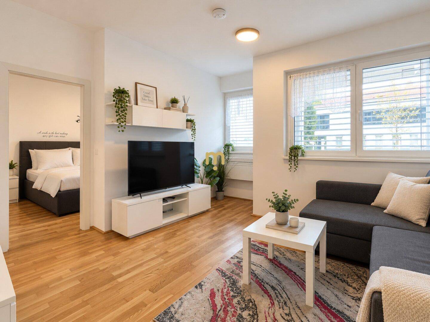 Geräumiges Wohnzimmer mit Sofa, Fernseher und Blick auf ein angrenzendes Schlafzimmer.