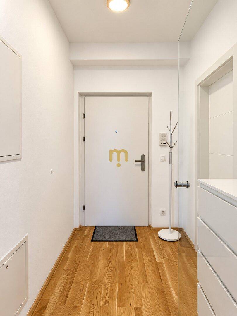 Heller Eingangsbereich mit Holzfußboden, weißer Tür und Garderobenständer.