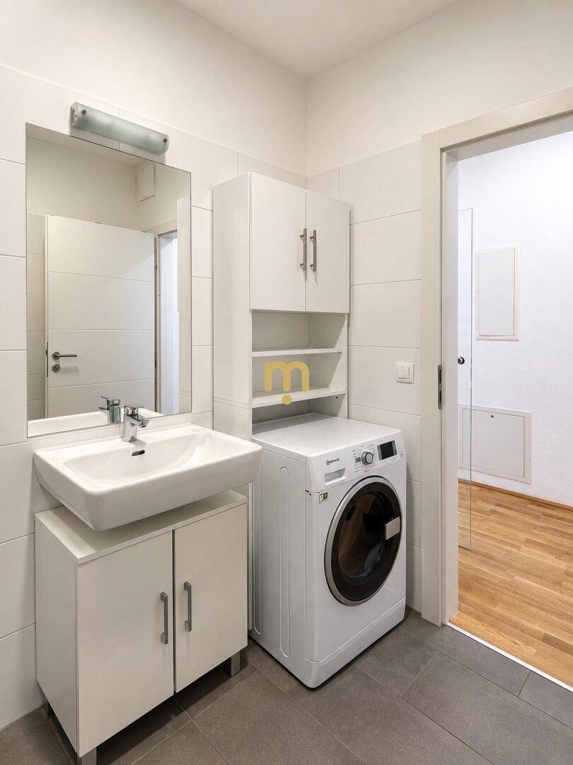 Helles Badezimmer mit Waschbecken, Spiegel, Waschmaschine und praktischen Hängeschränken.