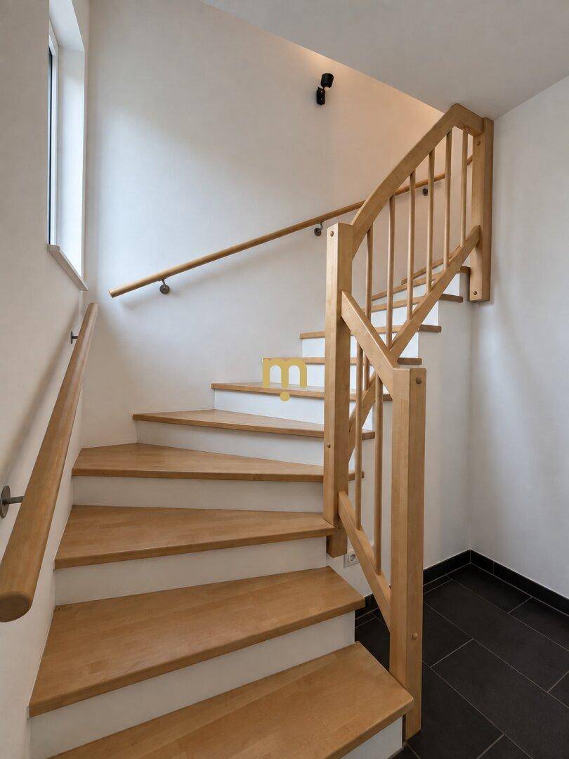 Holztreppe mit hellem Geländer und Stufen, die in die obere Etage führen.