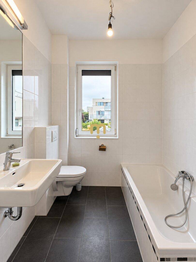 Modernes Badezimmer mit Badewanne, Waschbecken, WC und Fenster.