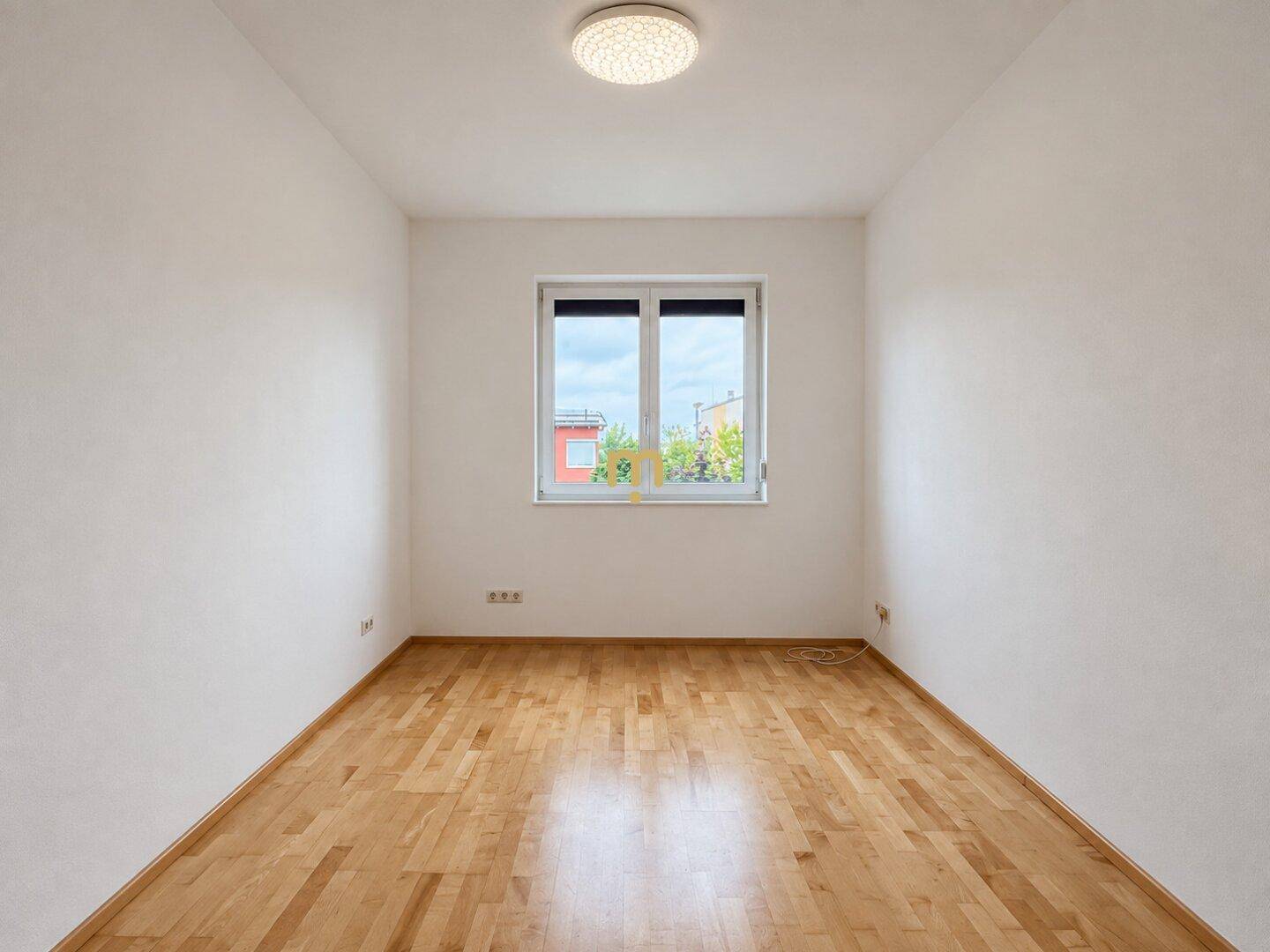 Leeres Zimmer mit Holzboden, weiß gestrichenen Wänden und einem Fenster.