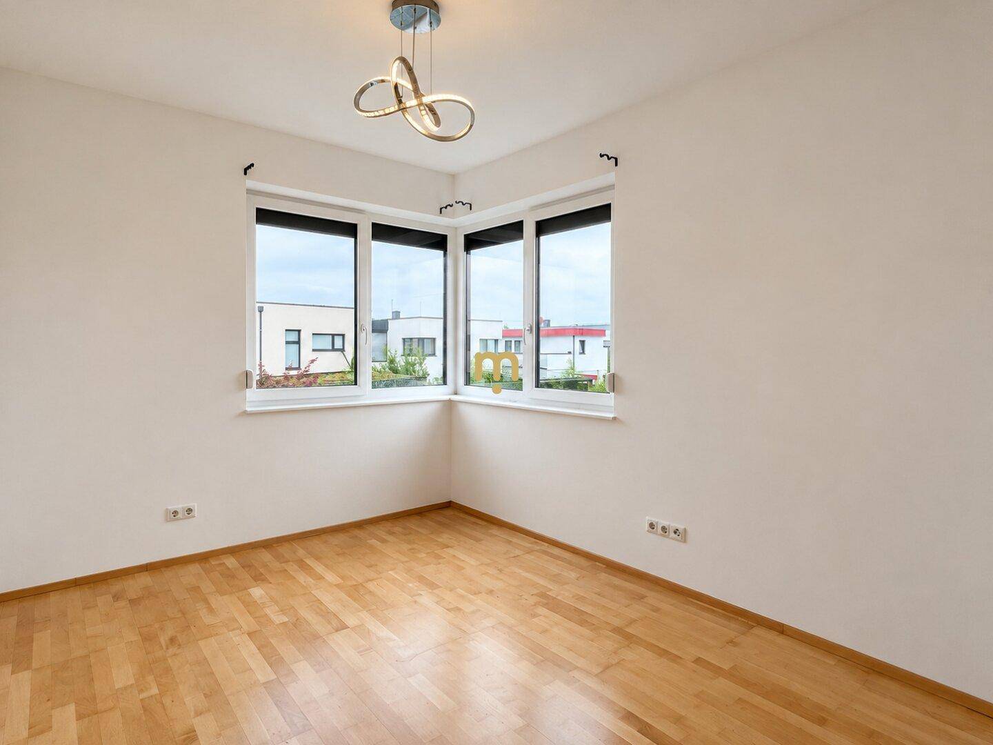 Helles Zimmer mit Holzboden, großen Fenstern und moderner Deckenleuchte.