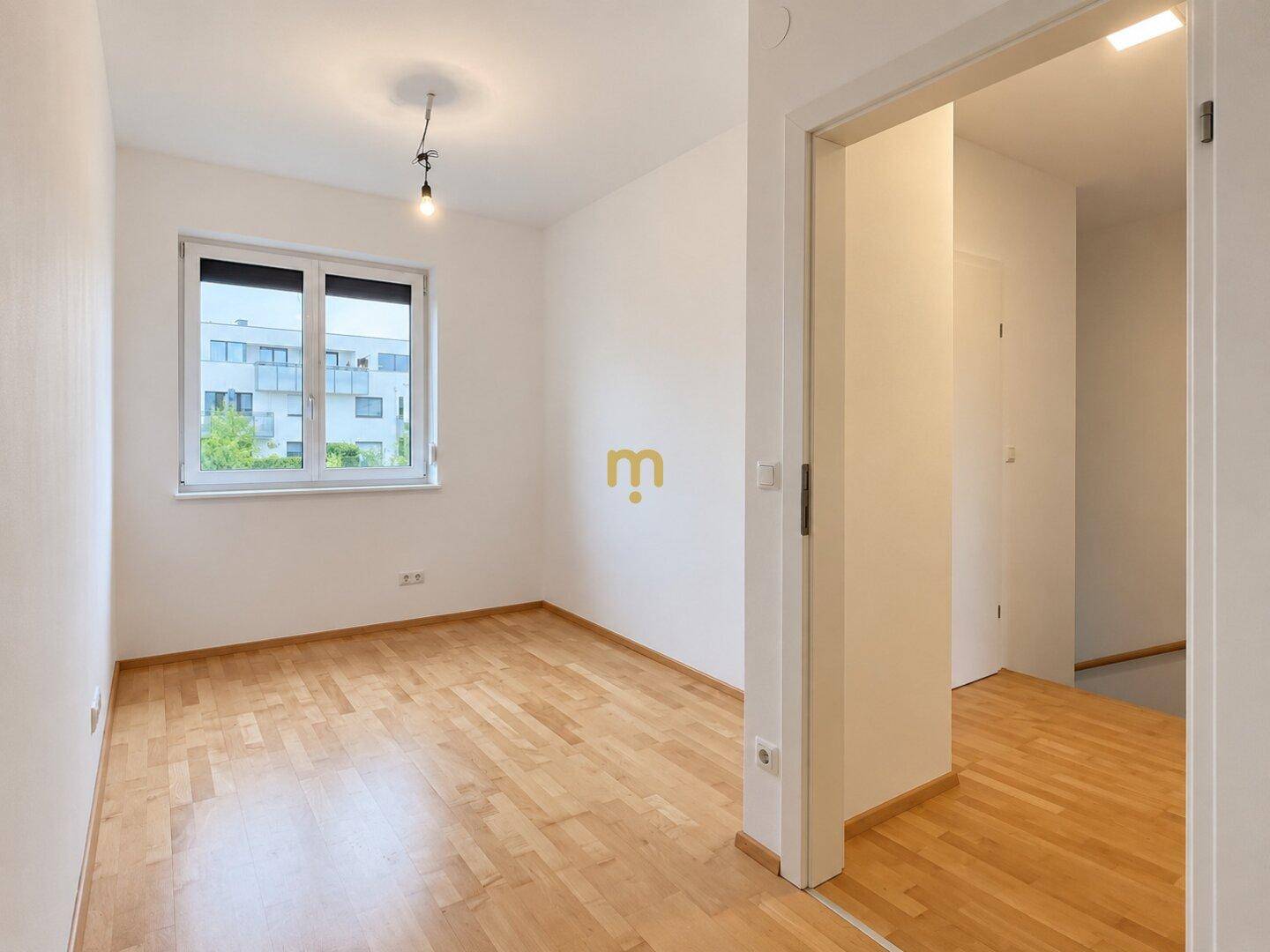 Geräumiges Zimmer mit Holzboden und Fenster, das viel Tageslicht hereinlässt.
