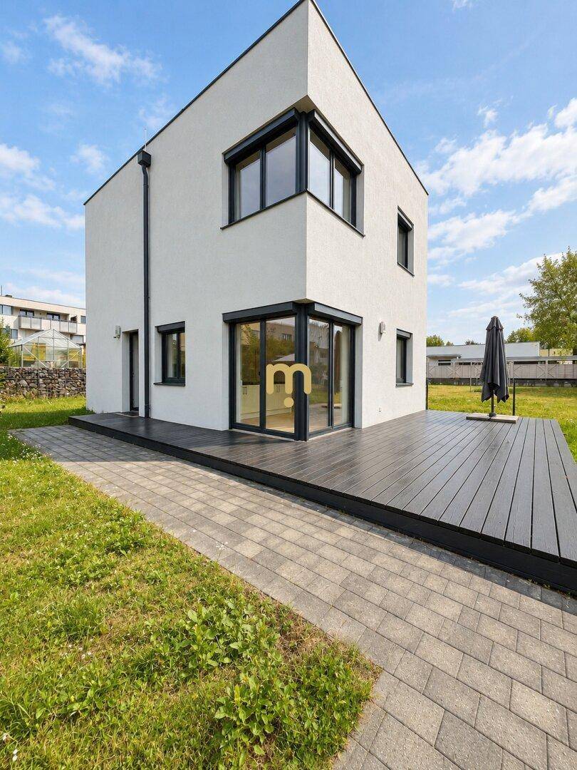 Seitliche Ansicht des Hauses mit großer Holzterrasse und angrenzender Rasenfläche.