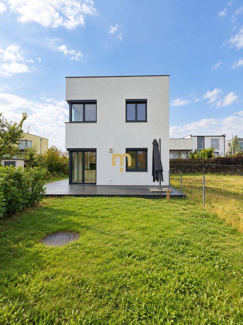 Hinteransicht des Hauses mit dunkler Holzterrasse und weitläufigem Rasenbereich.