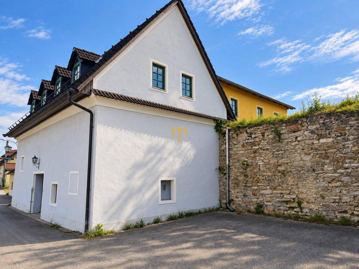 Seitenansicht des historischen Gebäudes mit einer alten Steinmauer und gepflastertem Vorplatz.