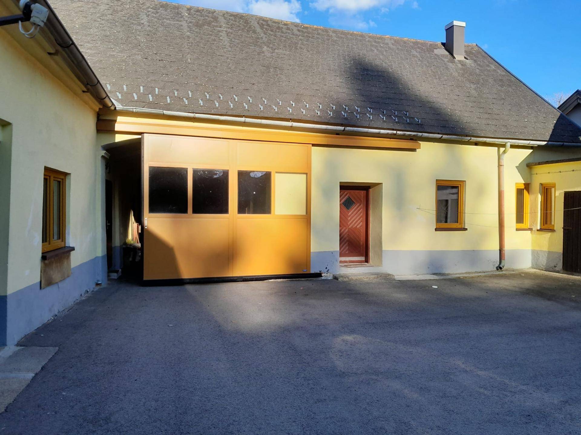 Innenhofbereich eines gelben Gebäudes mit großer Holztür und weiteren Fenstern, sonniger Tag.