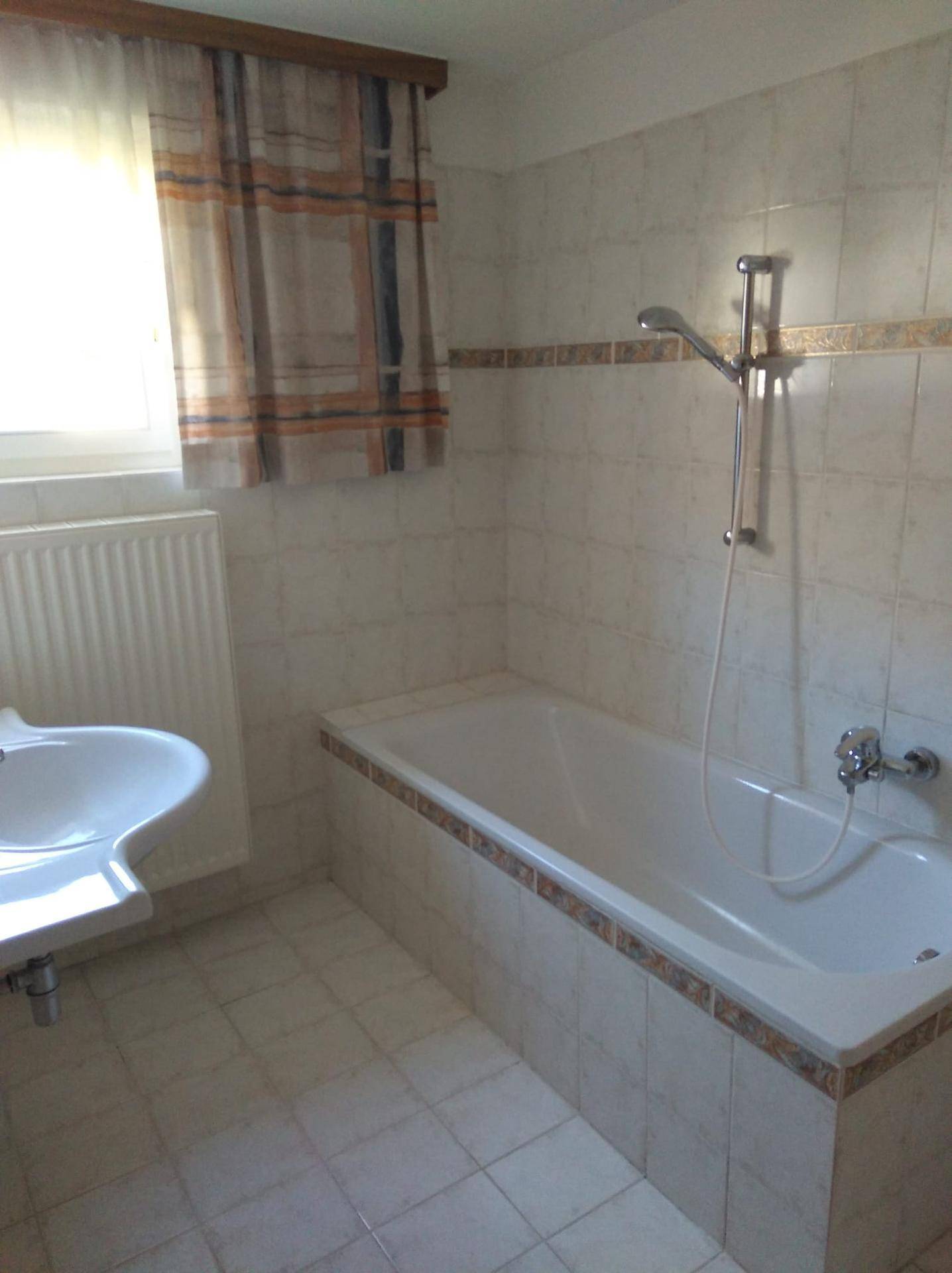 Badezimmer mit Badewanne, Waschbecken und hellen Fliesen, gut beleuchtet.