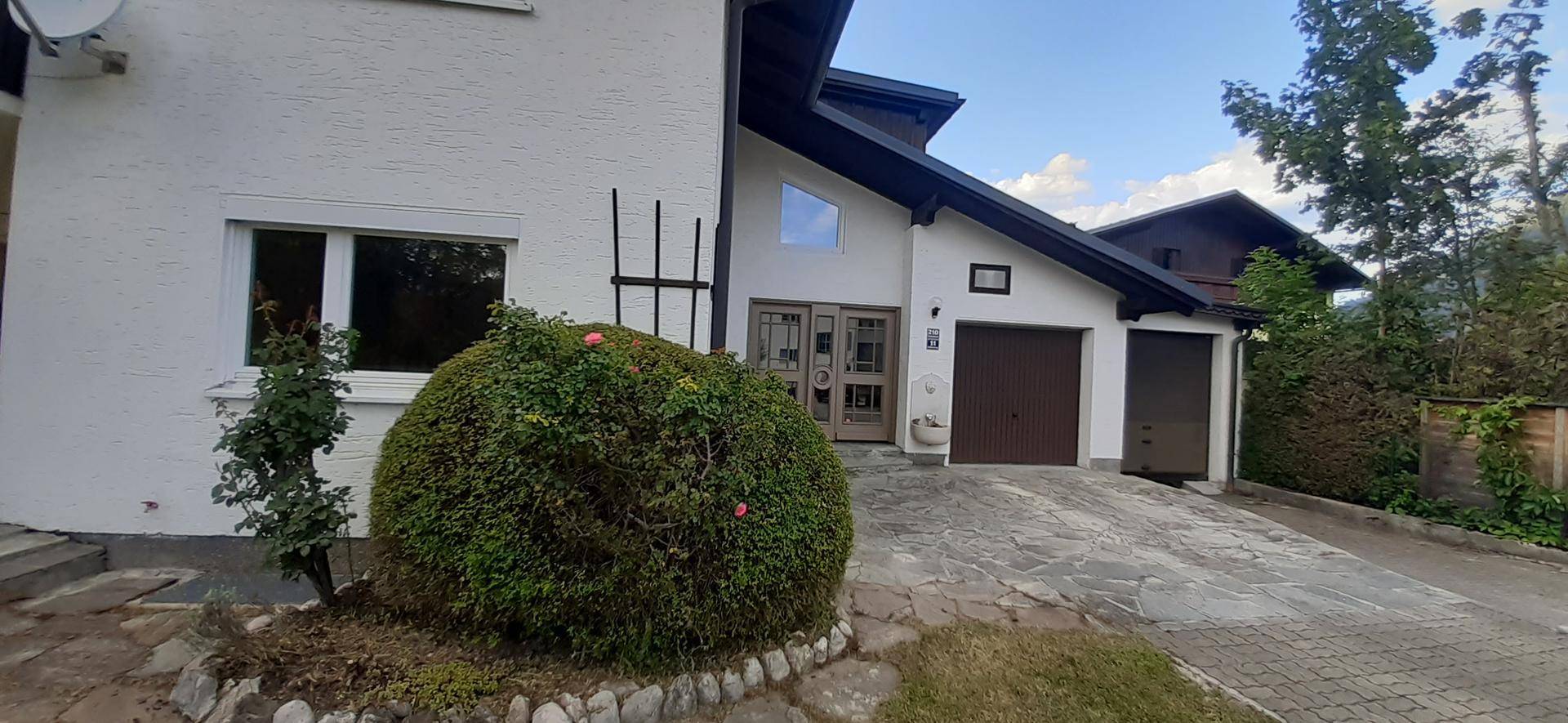 Vorderansicht des Hauses mit Einfahrt, Garage und gepflegter Bepflanzung.