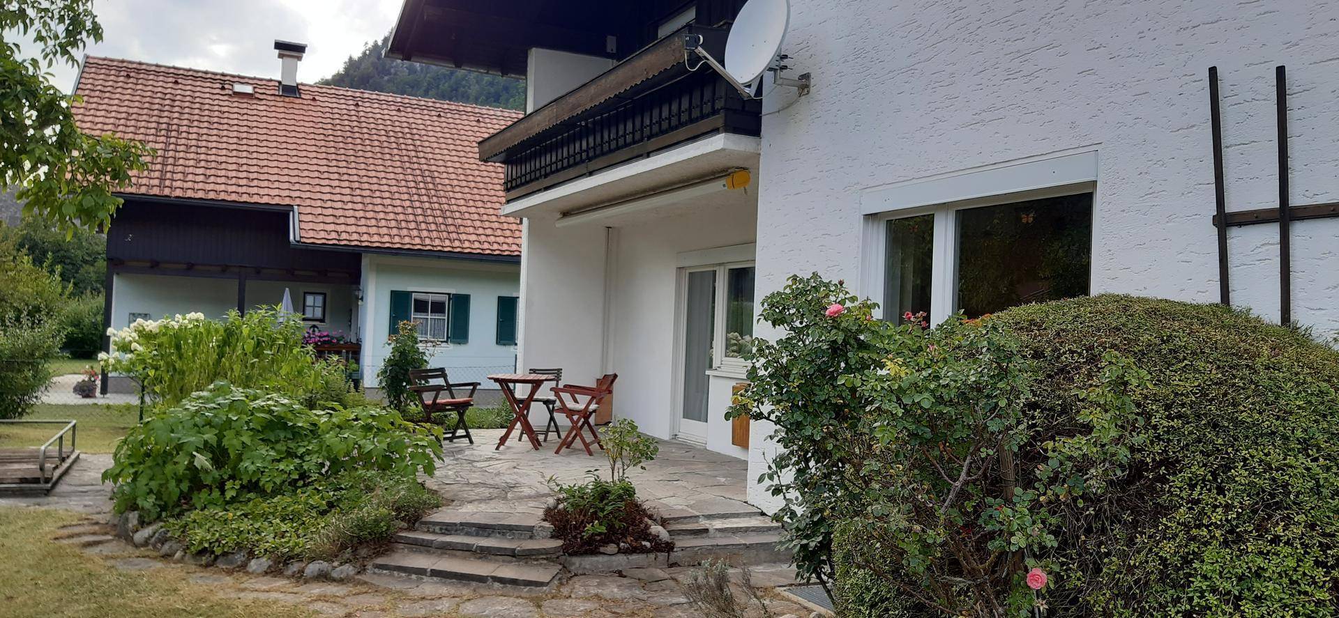 Seitliche Ansicht des Hauses mit gepflasterter Terrasse und üppiger Bepflanzung.