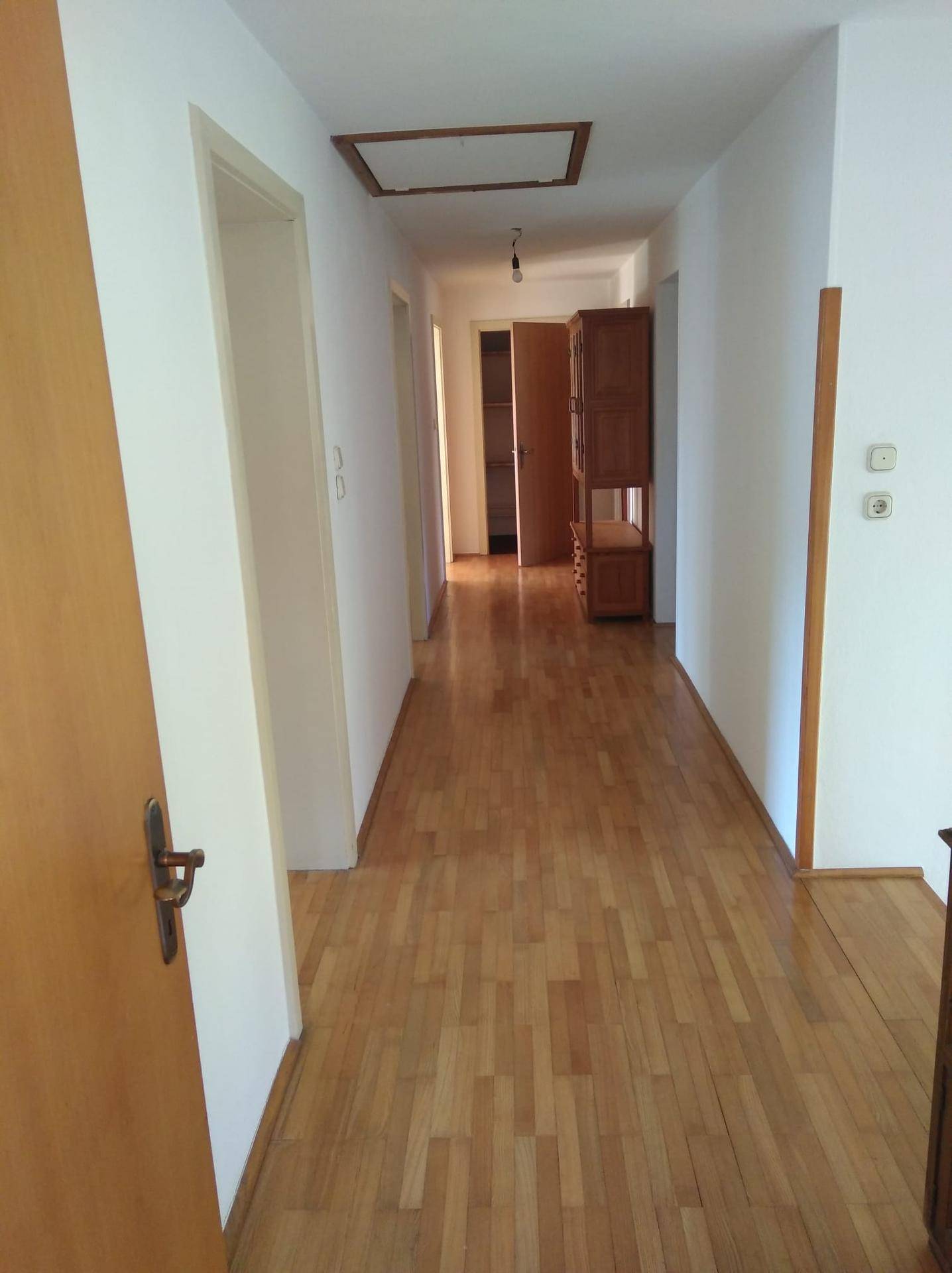 Langer Flur mit Holzboden, weißen Wänden und Türen zu verschiedenen Räumen.