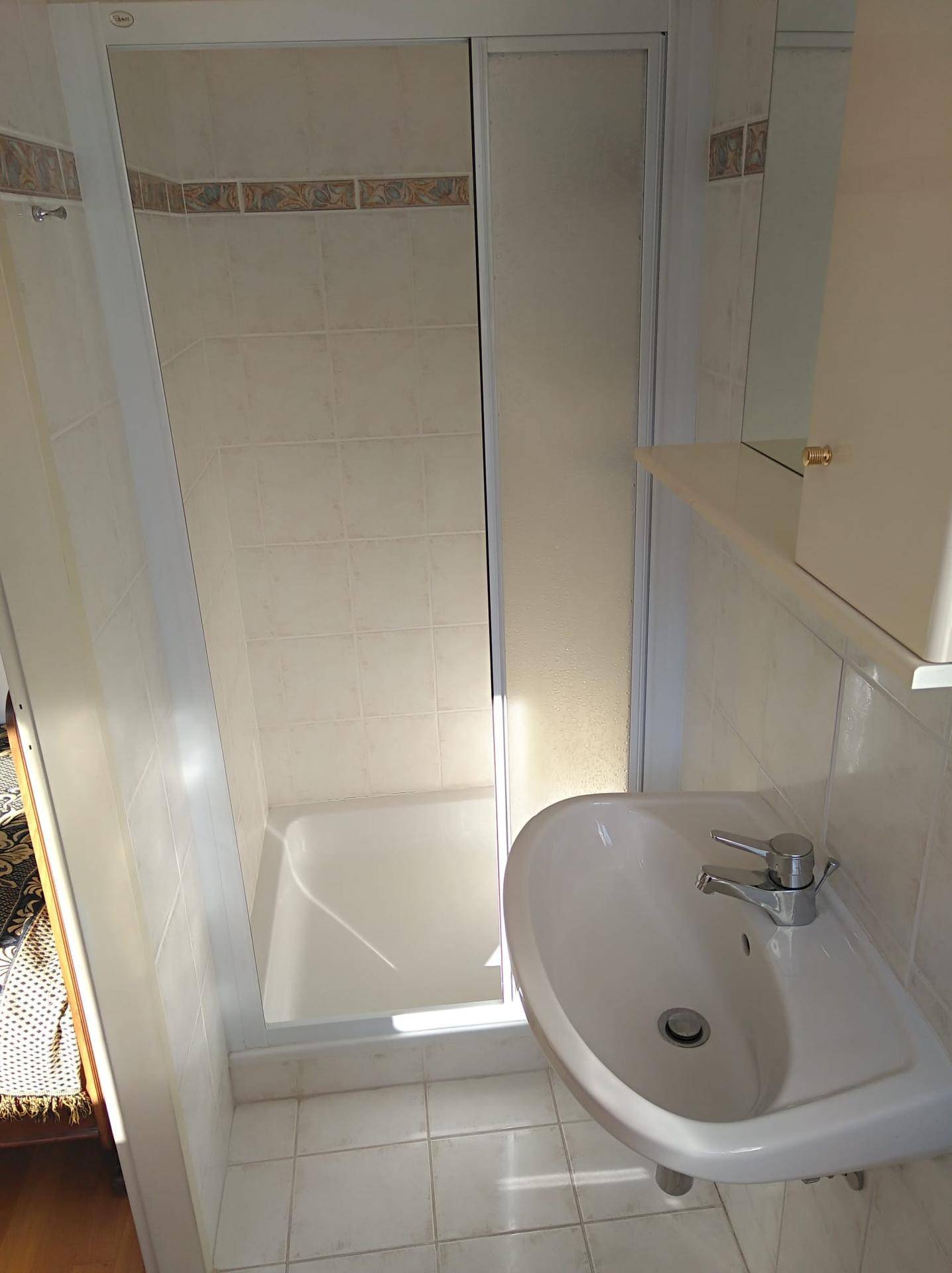 Kleines Badezimmer mit Duschkabine, Waschbecken und hellen Fliesen.