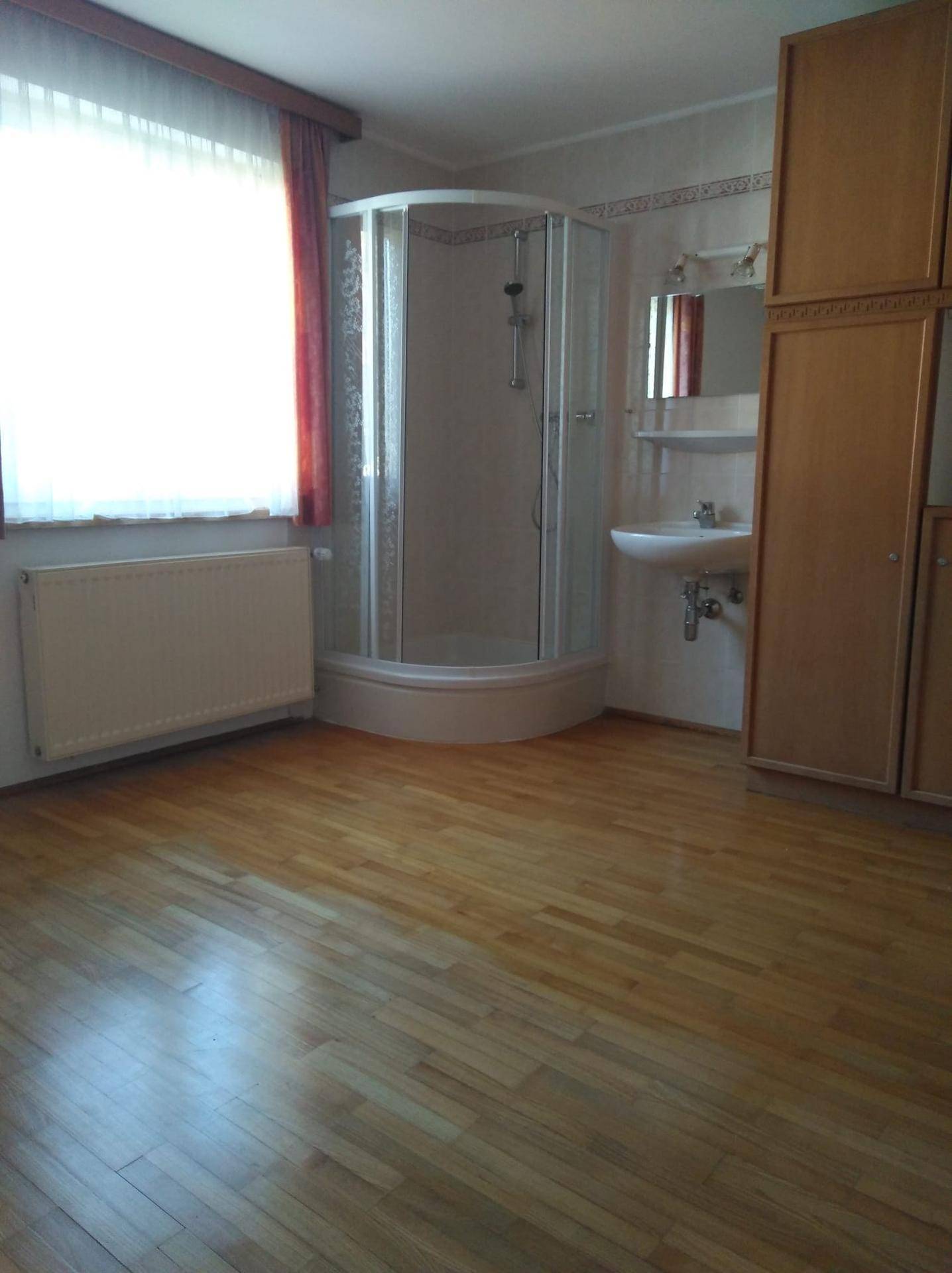 Badezimmer mit Duschkabine, Waschbecken und Holzschränken, hell durch Fenster.