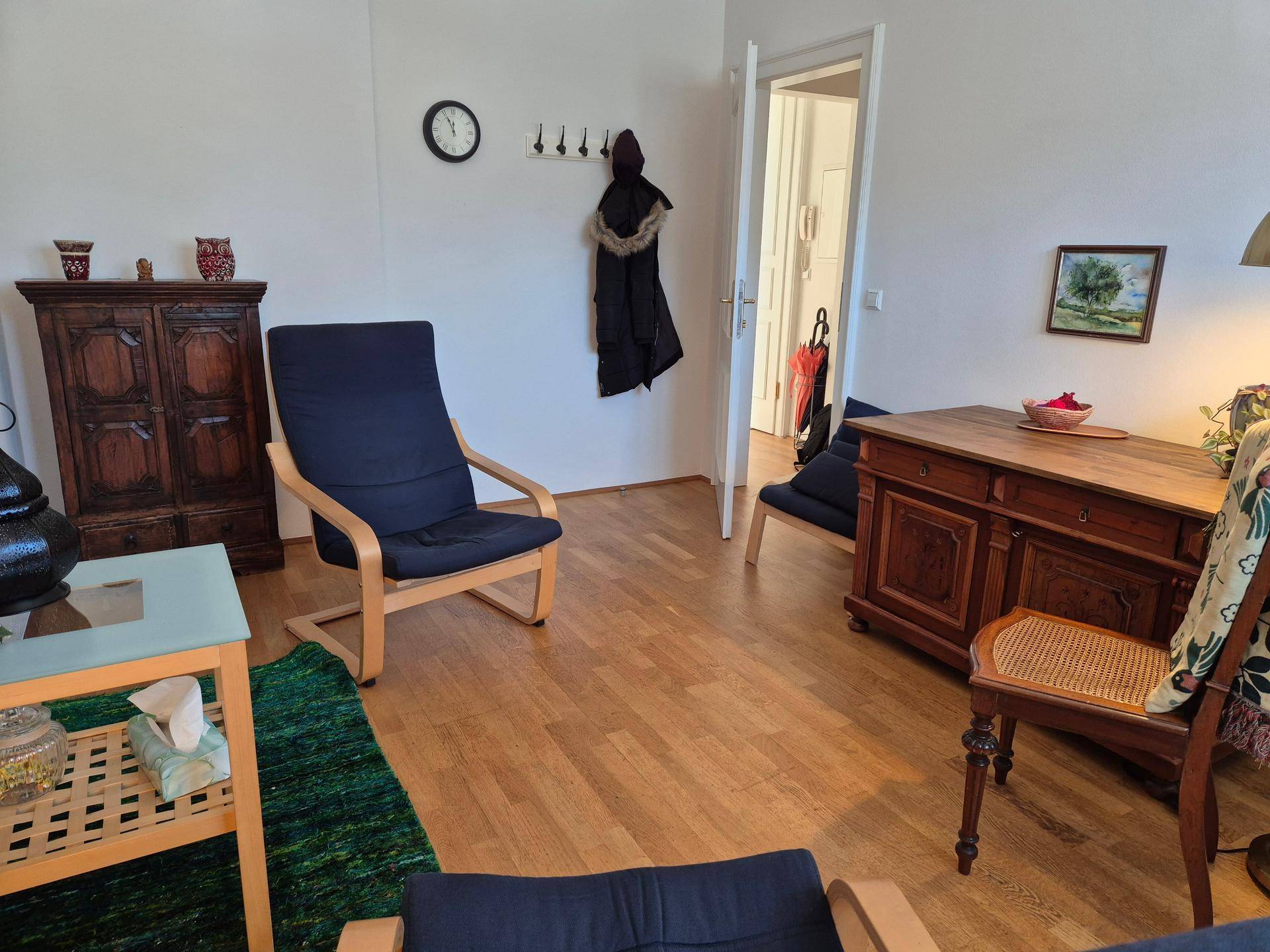 Geräumiger Wohnbereich mit Holzboden, traditionellen Möbeln und einem Durchgang zu einem weiteren Raum.