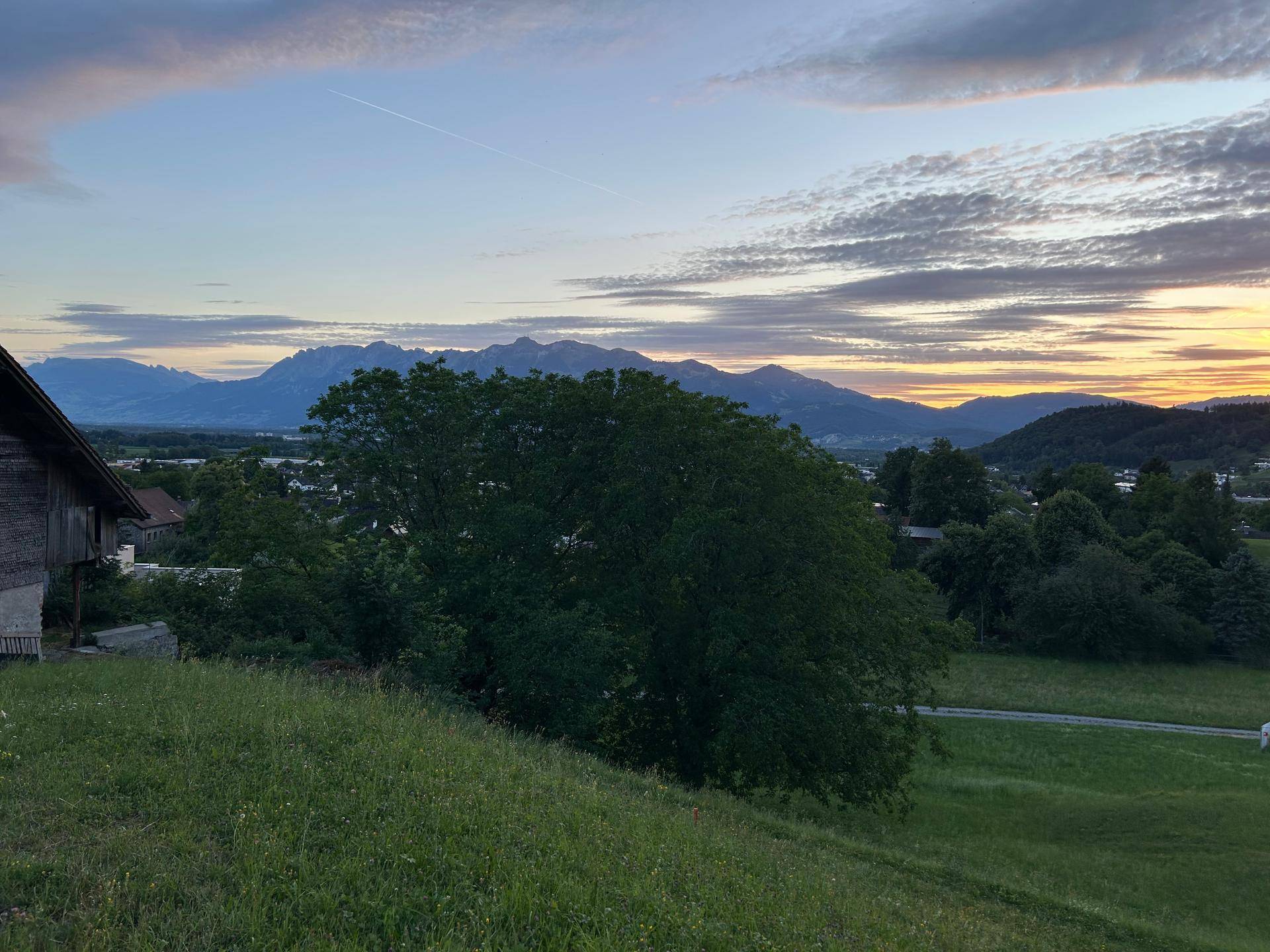 Weitläufige Landschaft mit Bergen, grünen Wiesen und einem malerischen Sonnenuntergang am Horizont.