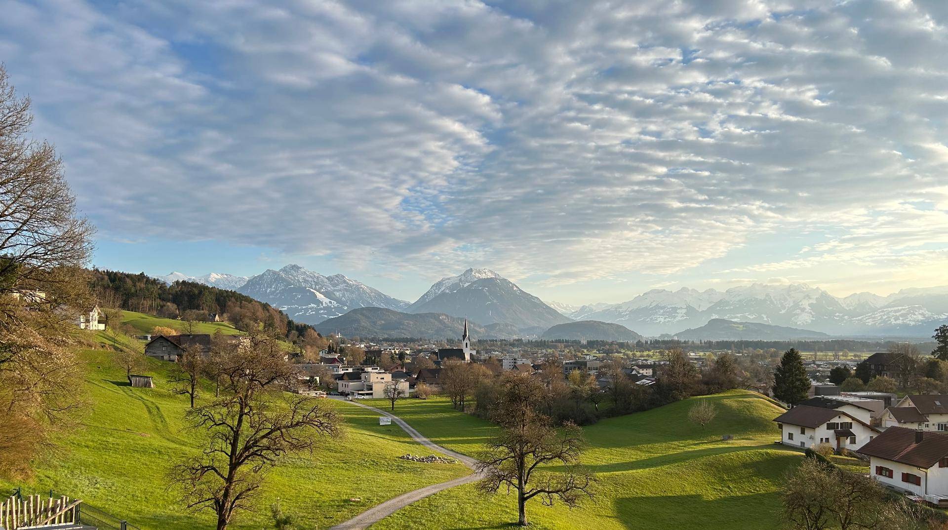 Weitläufiger Blick auf ein malerisches Dorf mit schneebedeckten Bergen unter einem bewölkten Himmel.