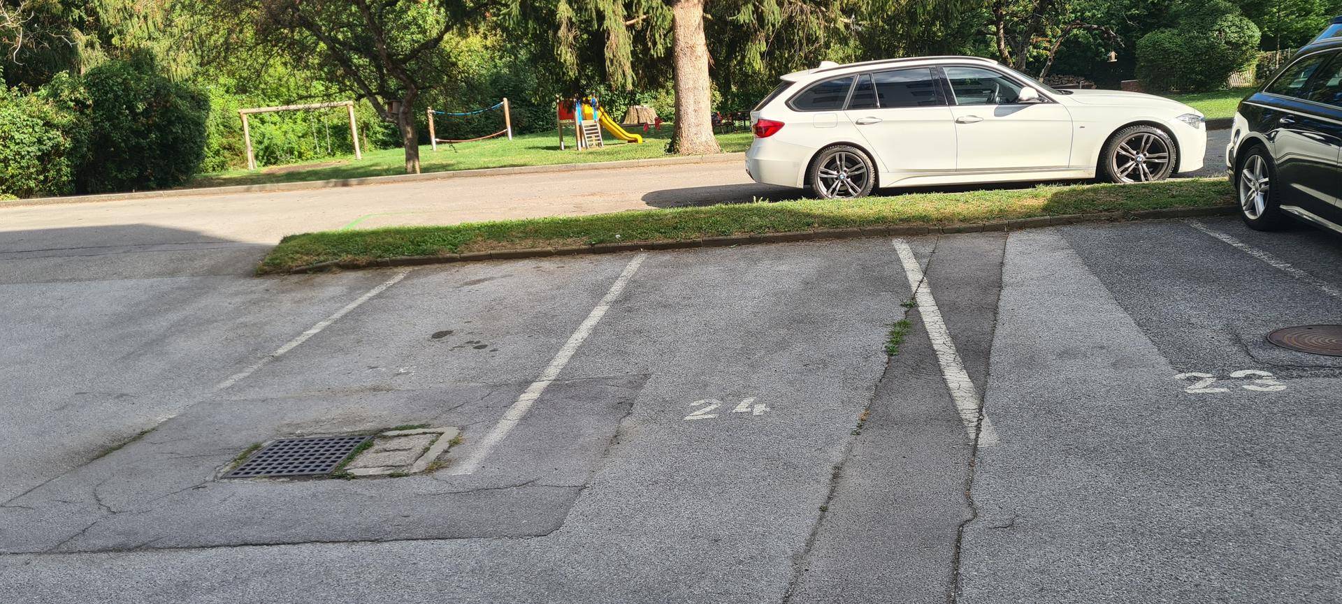 Außenparkplatz mit nummerierten Stellplätzen und einem Spielbereich unter Bäumen im Hintergrund.