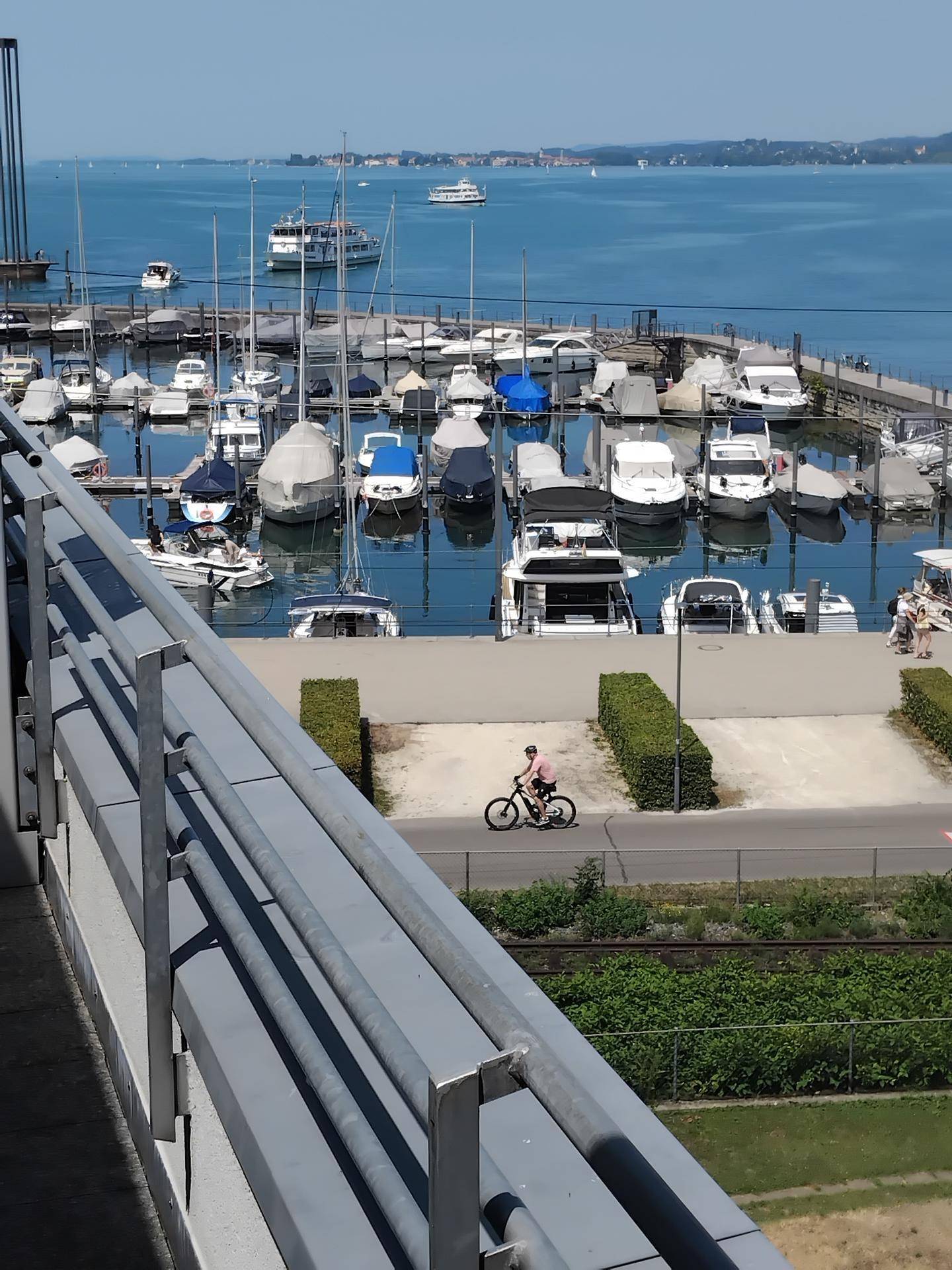 Blick vom Balkon auf den Yachthafen mit vielen Booten und dem glitzernden See an einem sonnigen Tag.