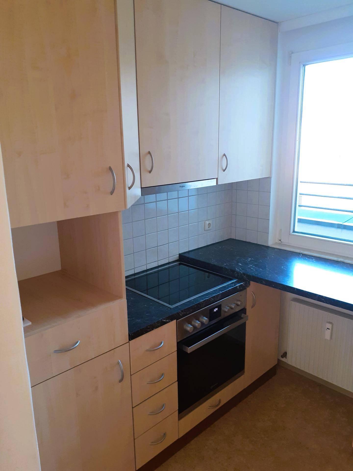 Funktionale Einbauküche mit hellen Holzschränken, dunkler Arbeitsplatte und integrierten Geräten.