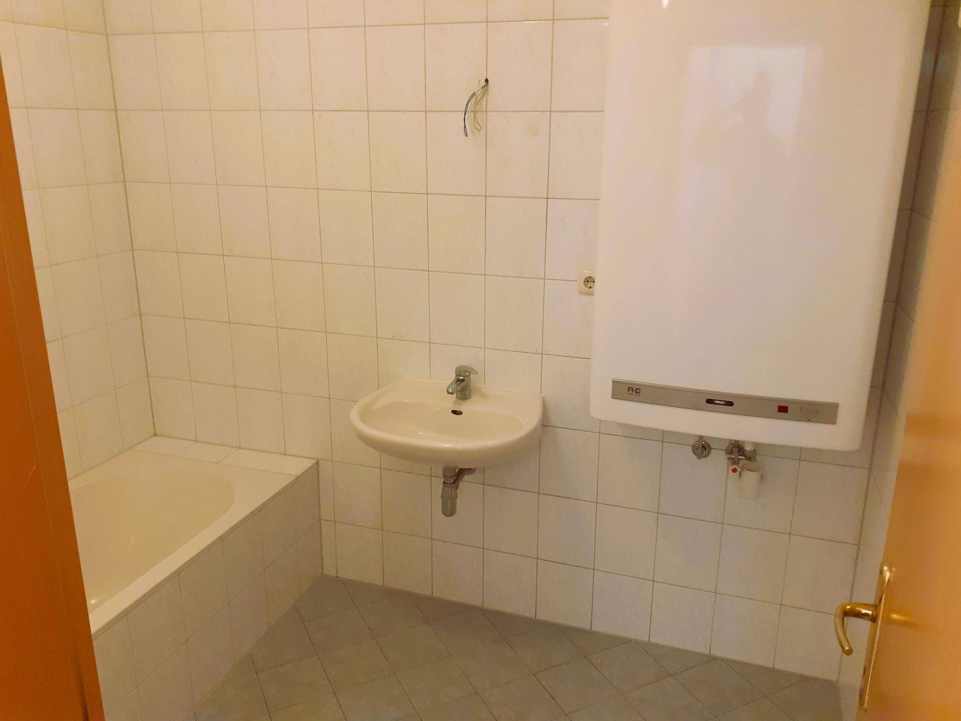 Badezimmer mit Badewanne, Waschbecken und weißen Wandfliesen, bereit zur individuellen Gestaltung.