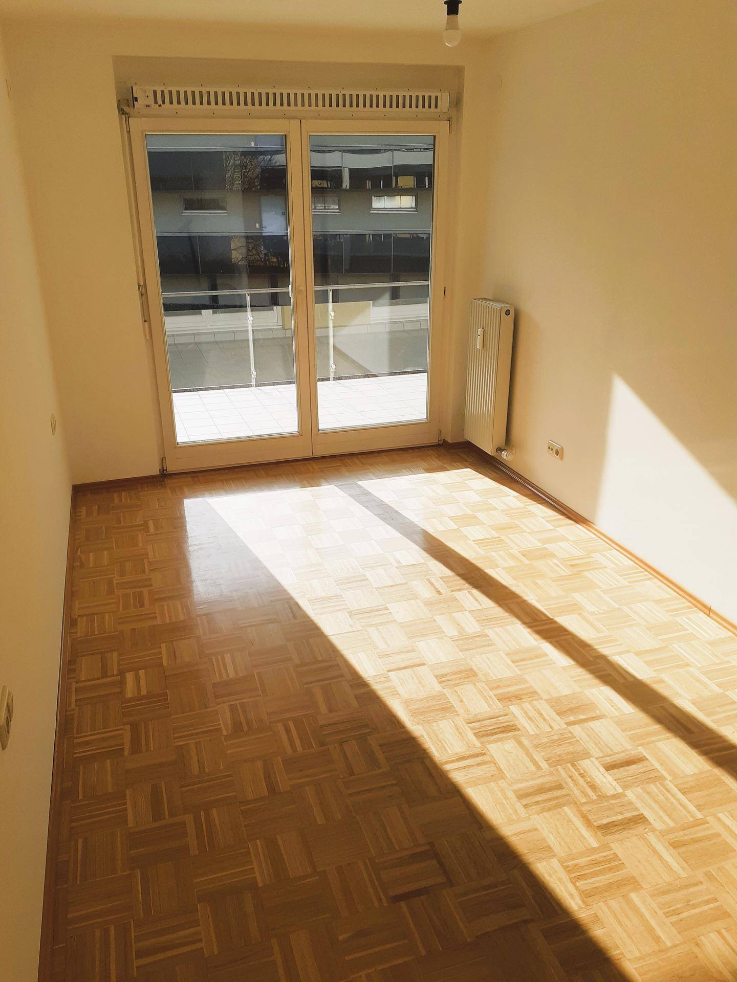 Sonniges Zimmer mit Parkettboden und Zugang zu einem Außenbereich, ideal für Entspannung.