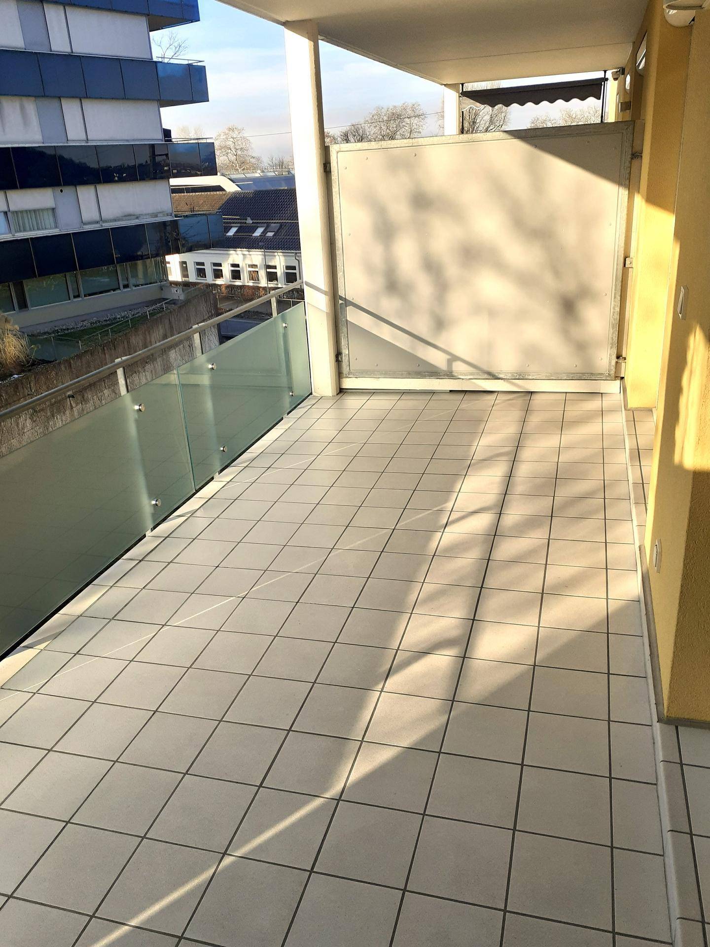Sonniger Balkon mit hellen Fliesen und einem modernen Glasgeländer, ideal zum Entspannen.