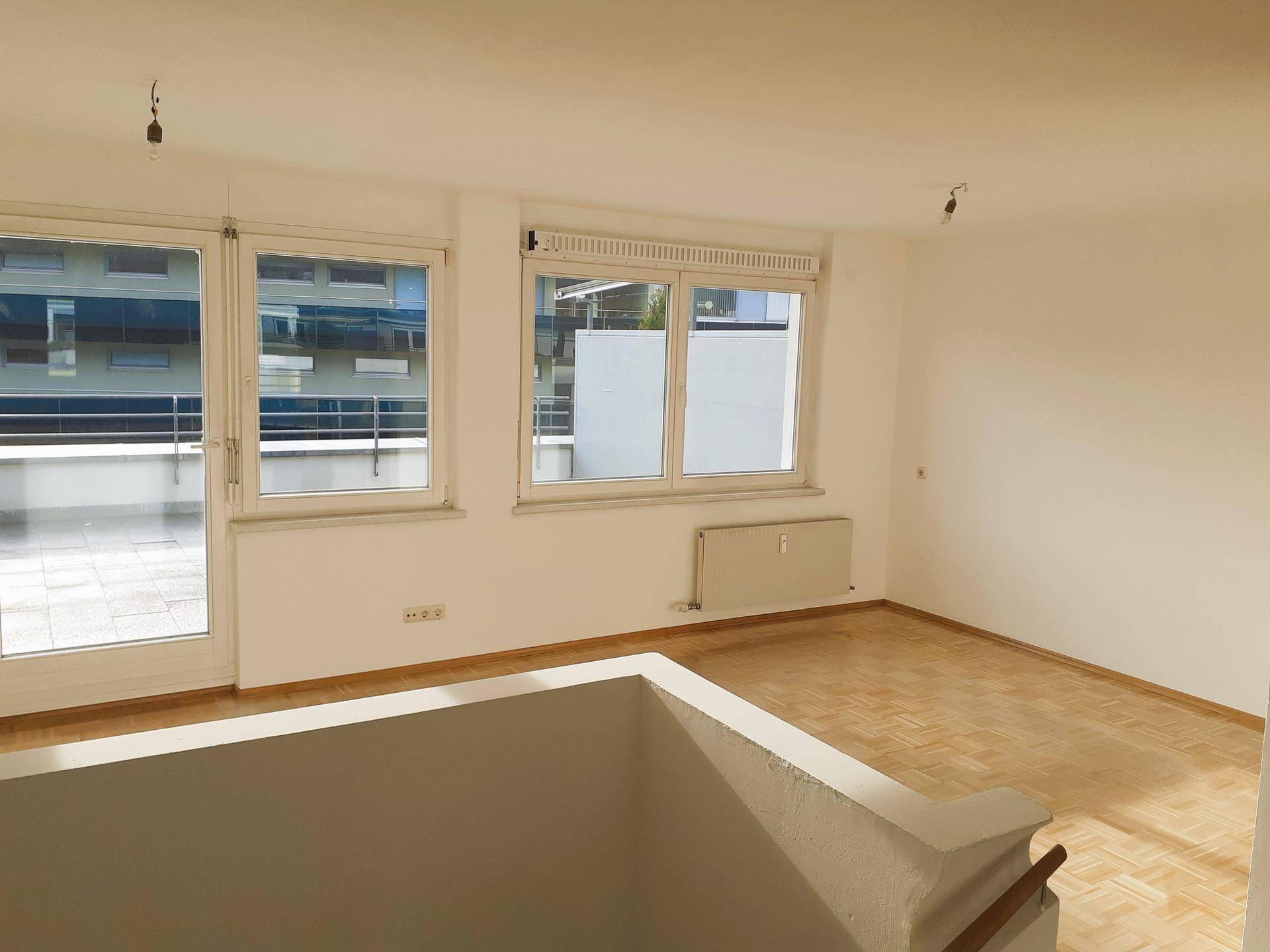 Lichtdurchfluteter Wohnraum mit Parkettboden und Blick auf den Außenbereich durch große Fenster.