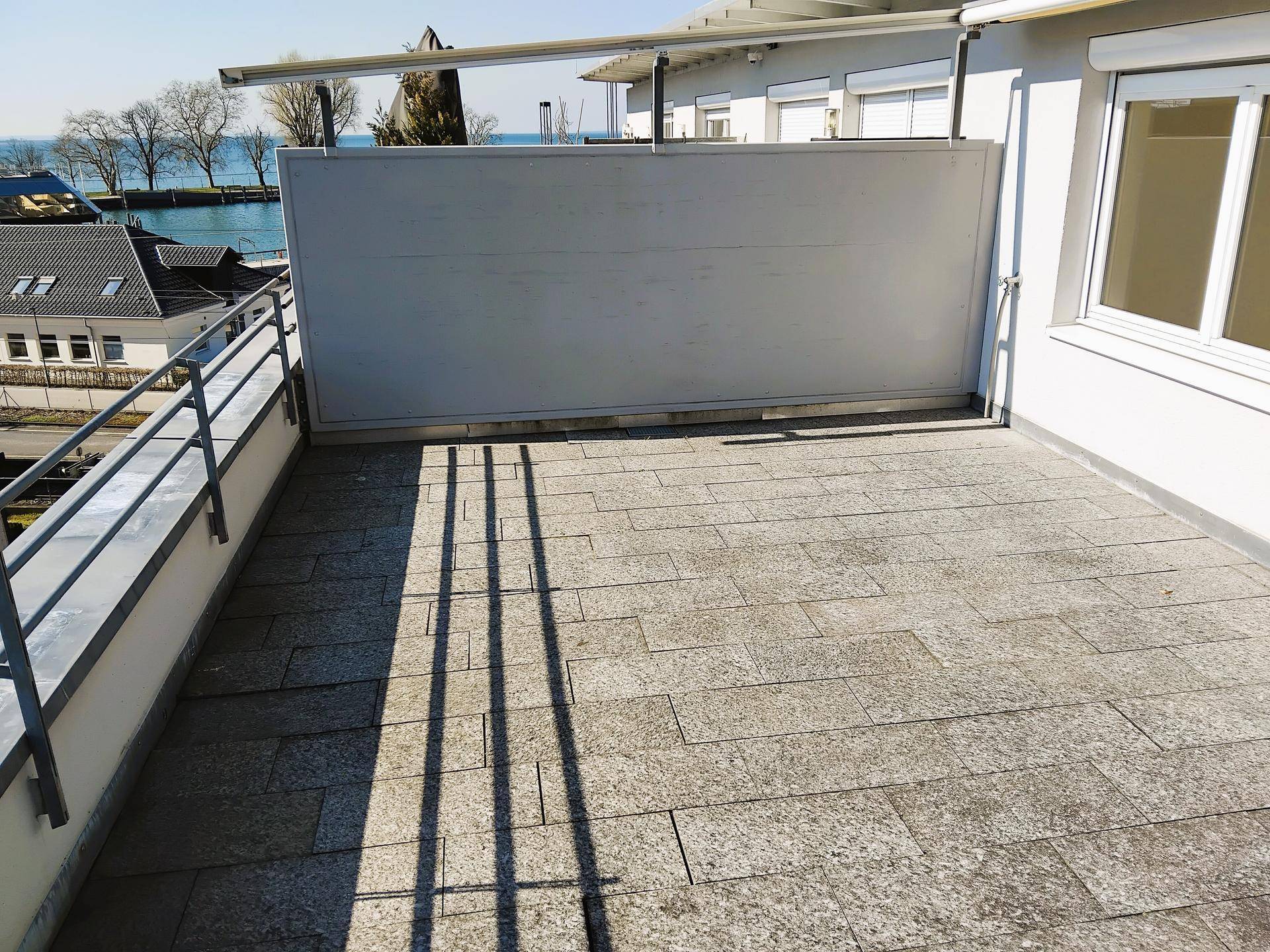 Sonnige Terrasse mit Steinplatten und einem Sichtschutz, die einen schönen Seeblick bietet.