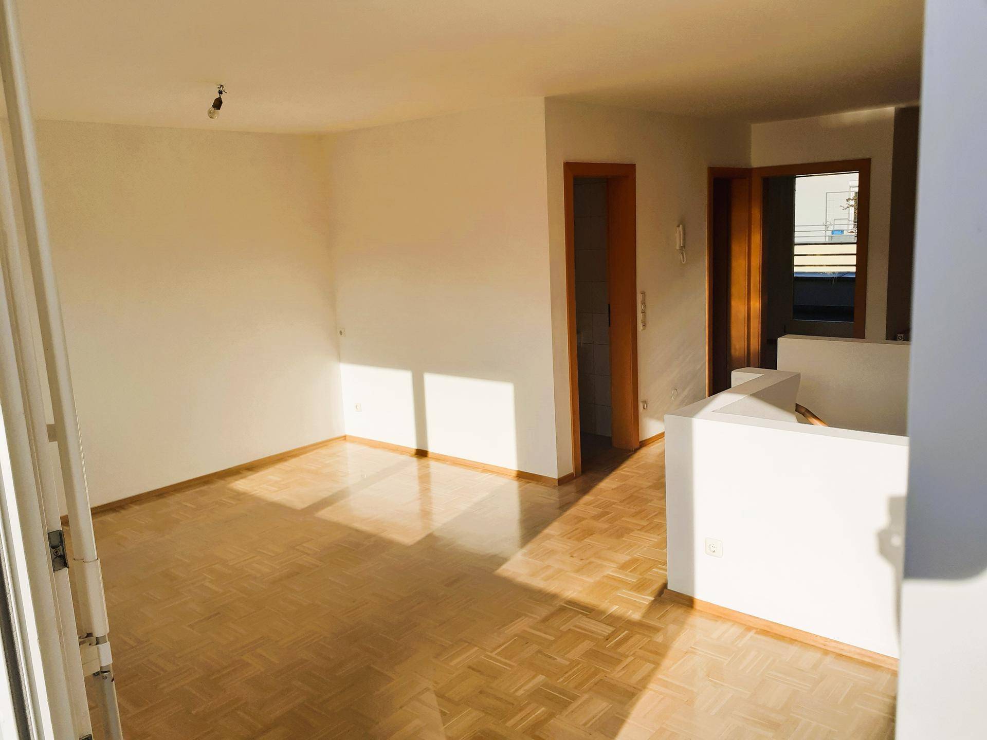 Sonniger Wohnbereich mit glänzendem Parkettboden und weiß gestrichenen Wänden, bereit zur Einrichtung.