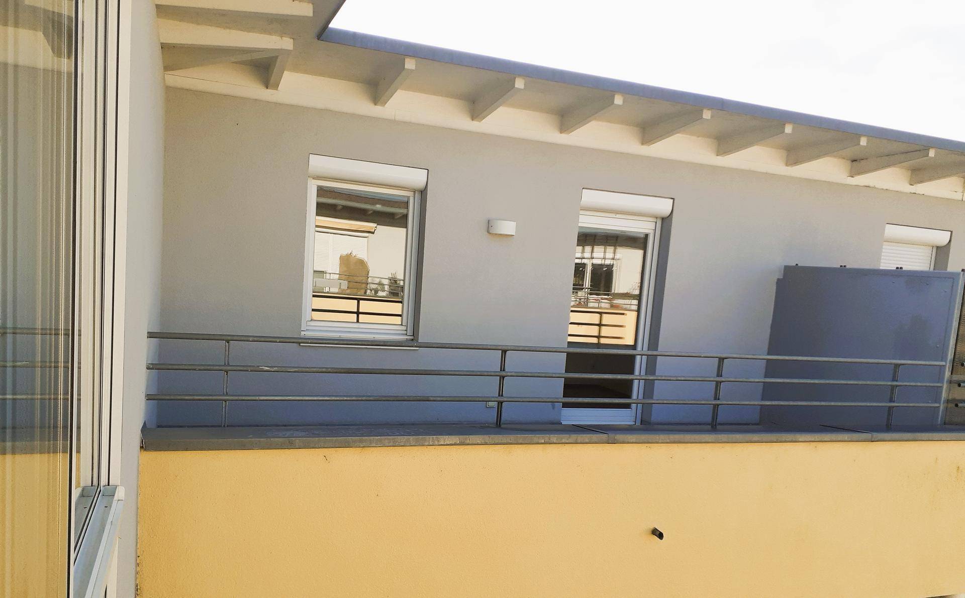 Fassade eines Gebäudes mit Fenstern, Rollläden und einem Balkongeländer in neutralen Farben.