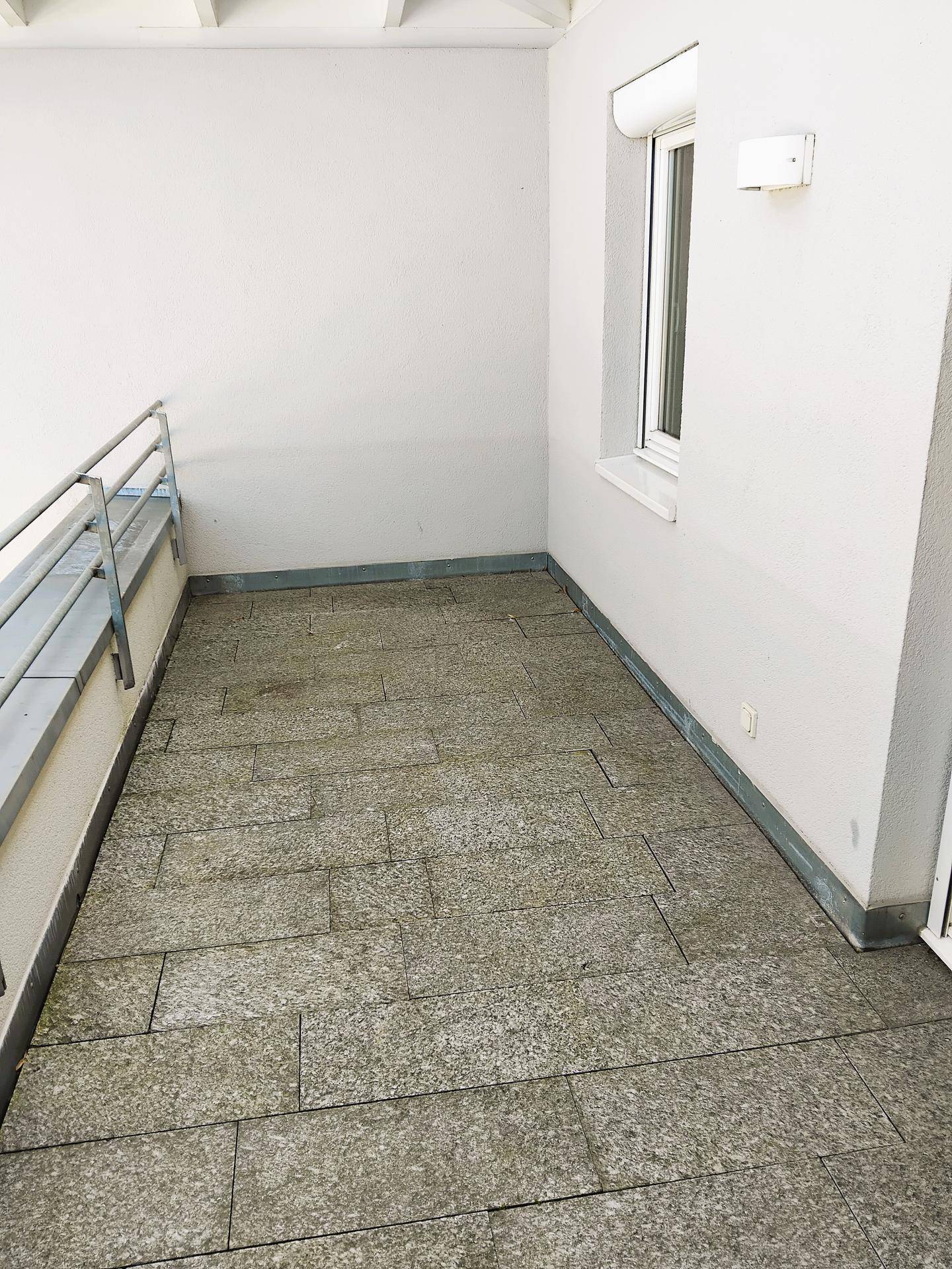 Kleiner Balkon mit Steinplattenboden und weiß gestrichenen Wänden, ideal für einen ruhigen Rückzugsort.