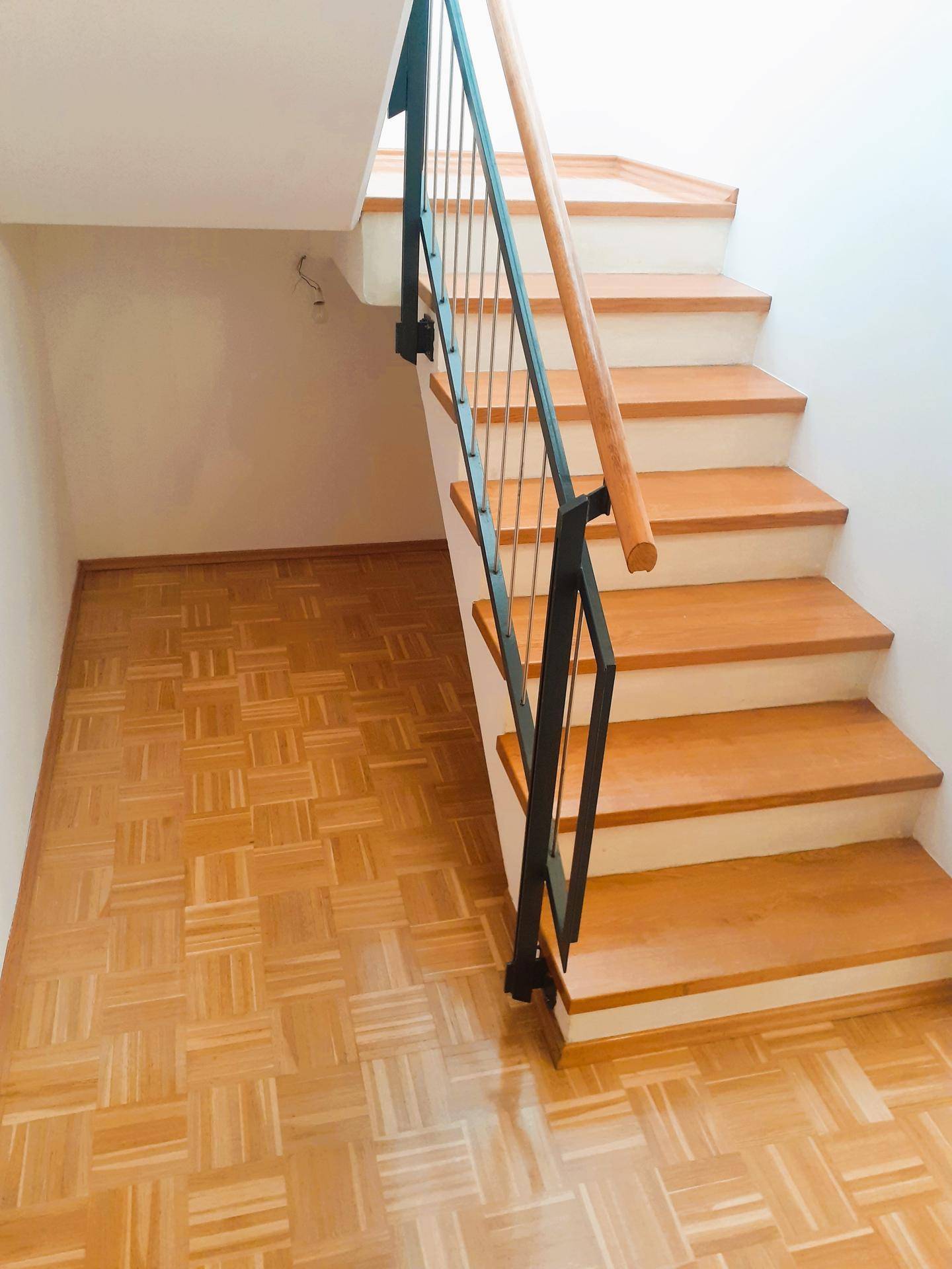 Holztreppe mit modernem Metallgeländer und Parkettboden, die die Etagen verbindet.