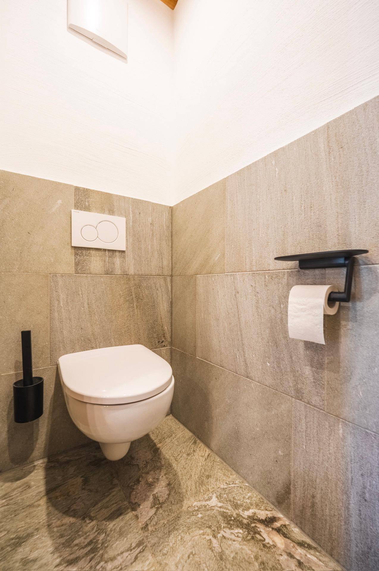 Separate Toilette mit Wand-WC und modernen Fliesen an den Wänden und auf dem Boden.