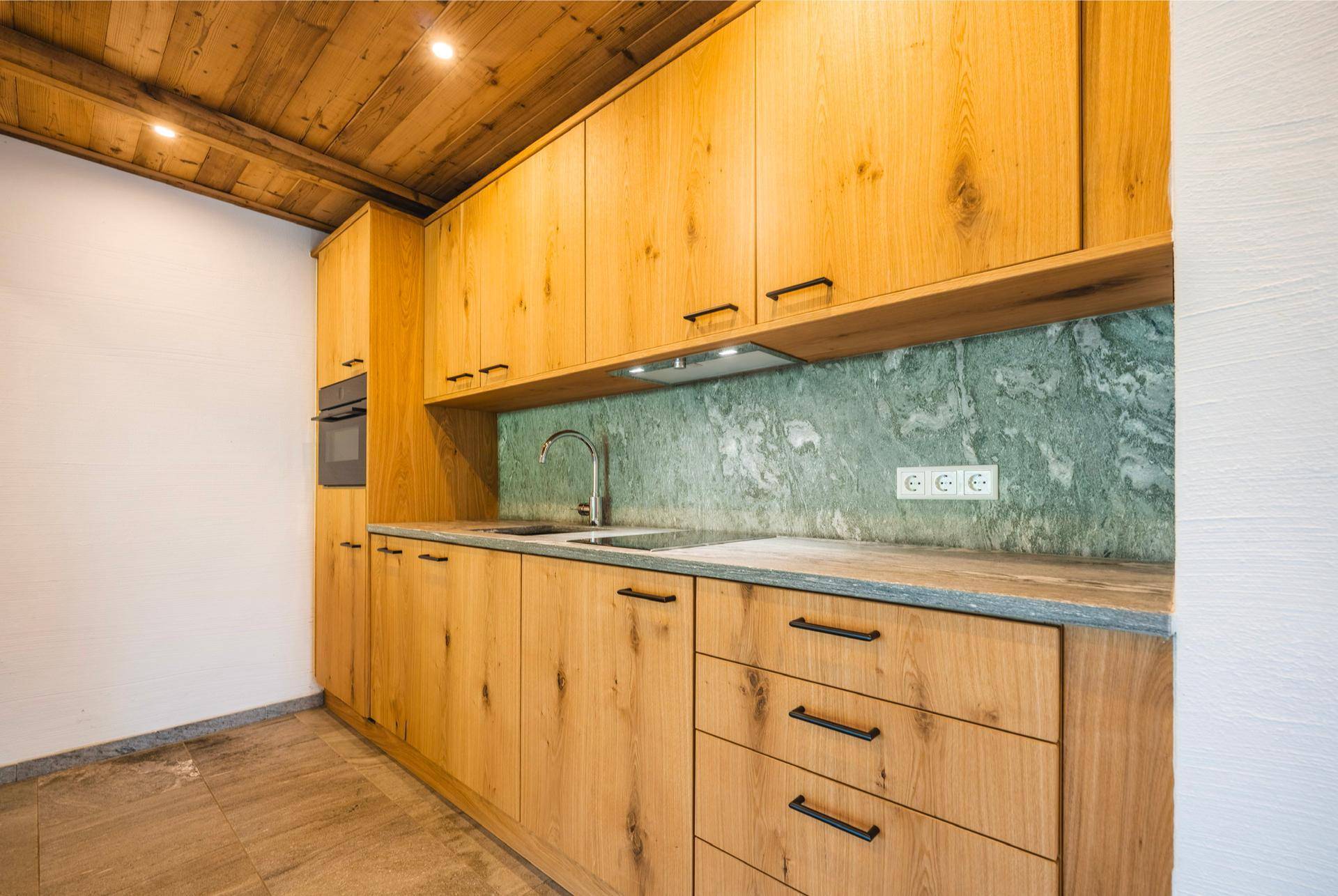 Voll ausgestattete Holzküche mit Einbaugeräten, Steinrückwand und viel Stauraum.