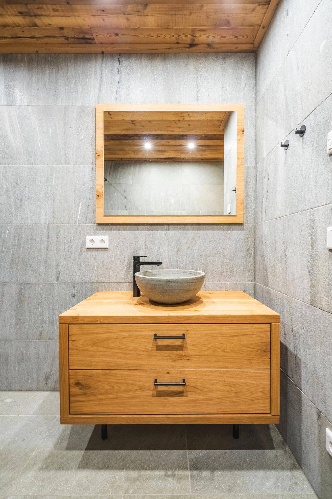 Modernes Badezimmer mit Holzwaschtisch, Aufsatzbecken und großem Spiegel an gefliesten Wänden.