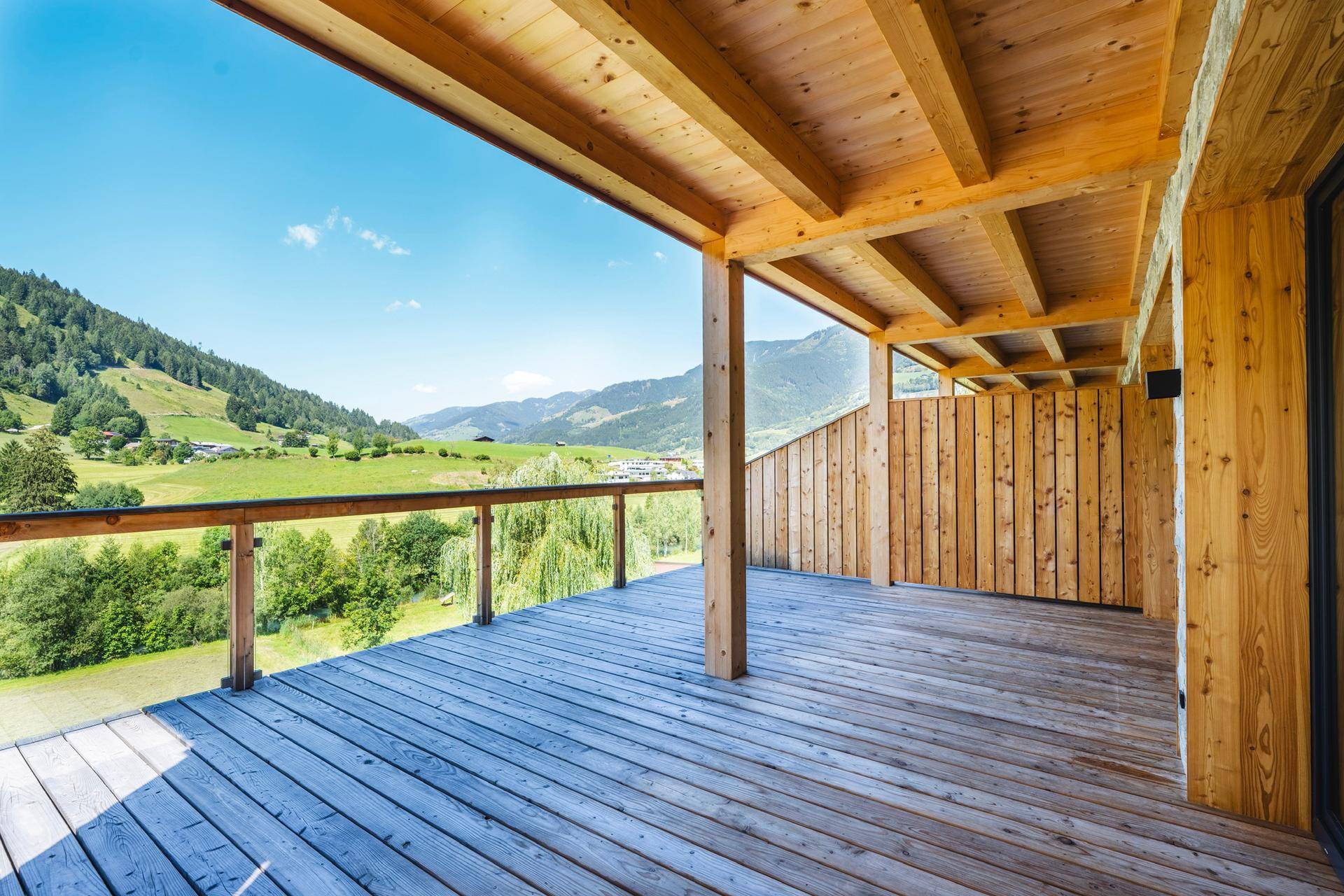 Großer überdachter Holzbalkon mit weitem Blick auf die grüne Berglandschaft und viel Sonne.