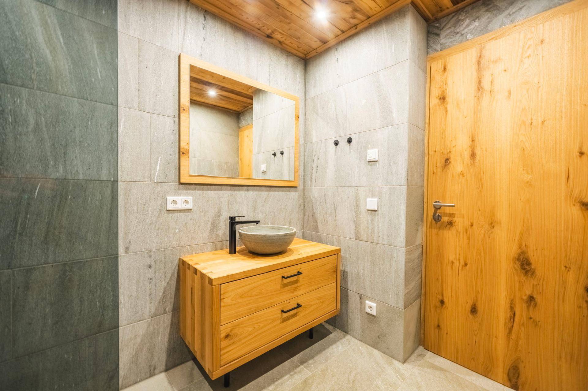 Modernes Badezimmer mit Holzwaschtisch, Aufsatzbecken und großem Spiegel an gefliesten Wänden.