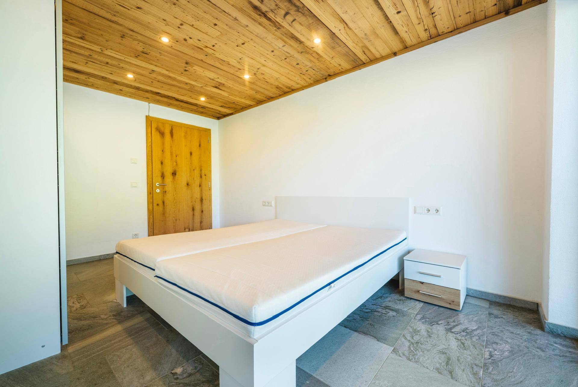 Helles Schlafzimmer mit Holzbalkendecke, Fliesenboden und schlichtem, modernem Design.