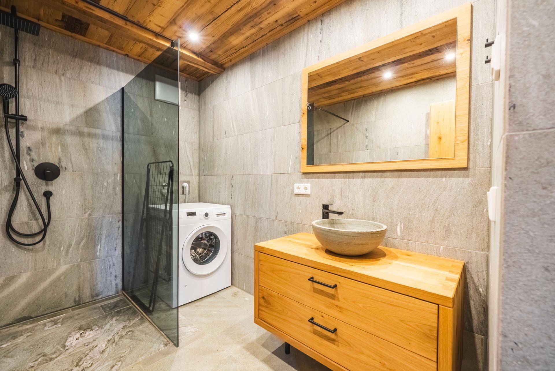 Modernes Badezimmer mit begehbarer Dusche, Waschmaschine und Holzwaschtisch mit Aufsatzbecken.