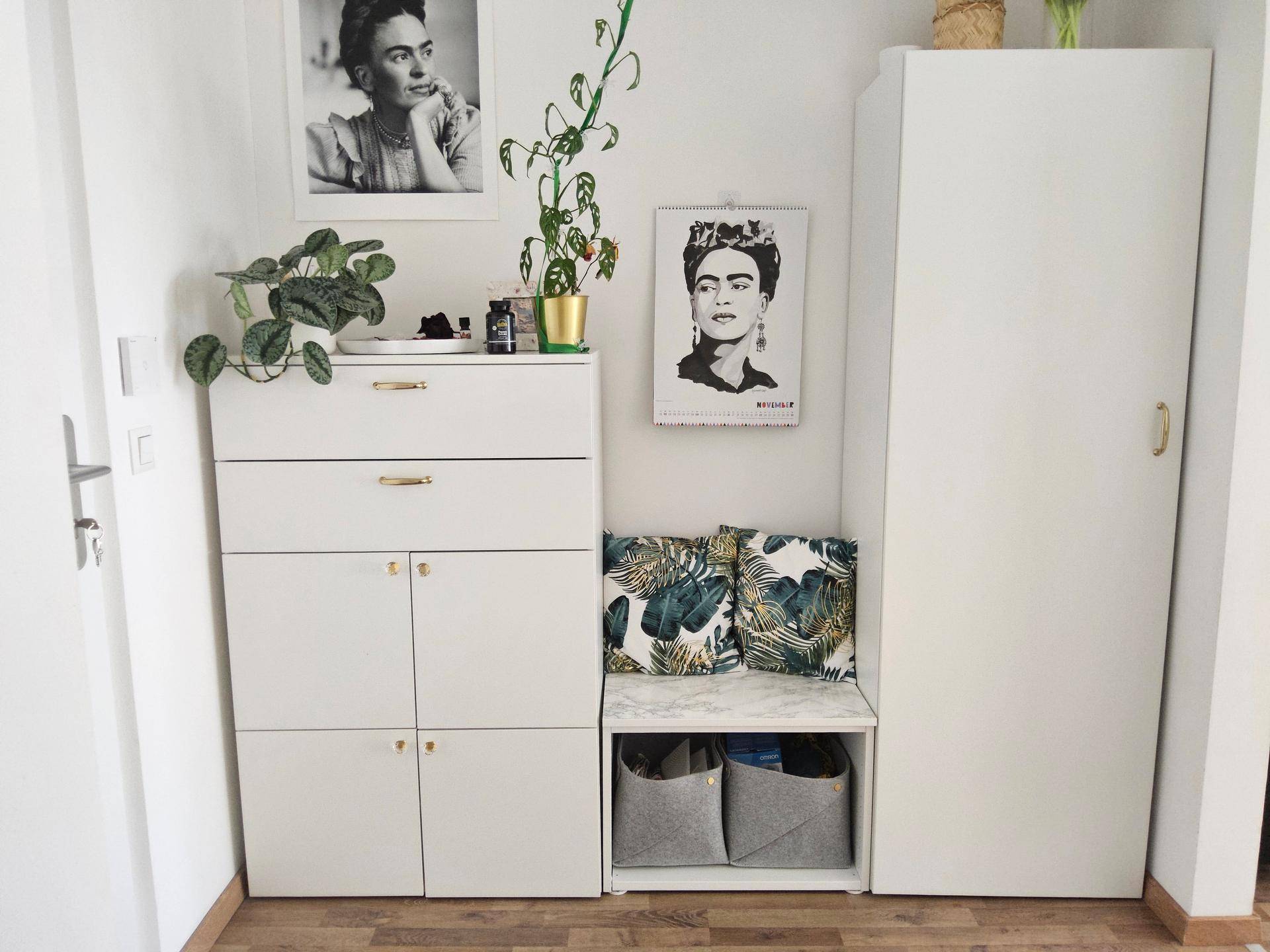 Heller Eingangsbereich mit weißen Schuhschränken, Sitzbank und dekorativen Bildern an der Wand.