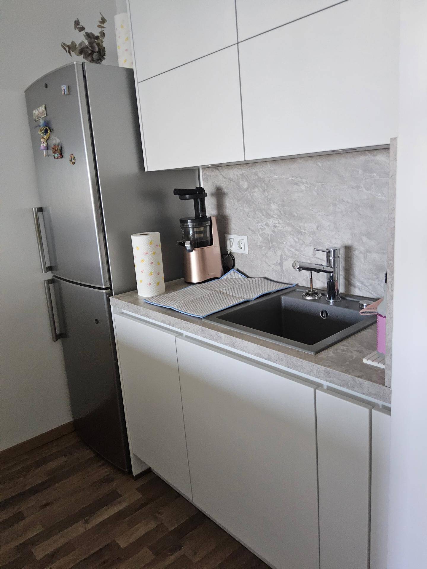 Helle Küche mit weißen Unterschränken, Spülbecken und einem großen Kühlschrank.